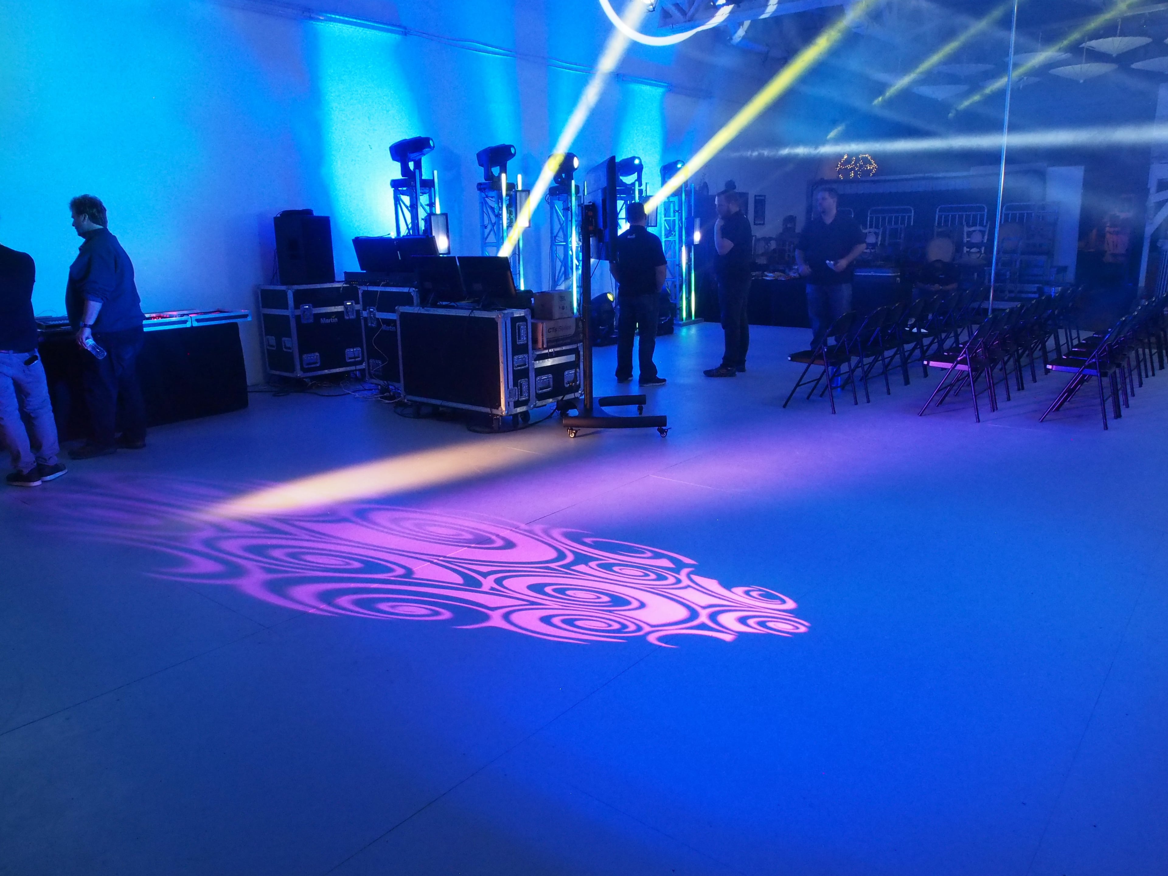 A spacious room set up for an event, featuring lighting equipment and rows of black chairs organized for attendees.