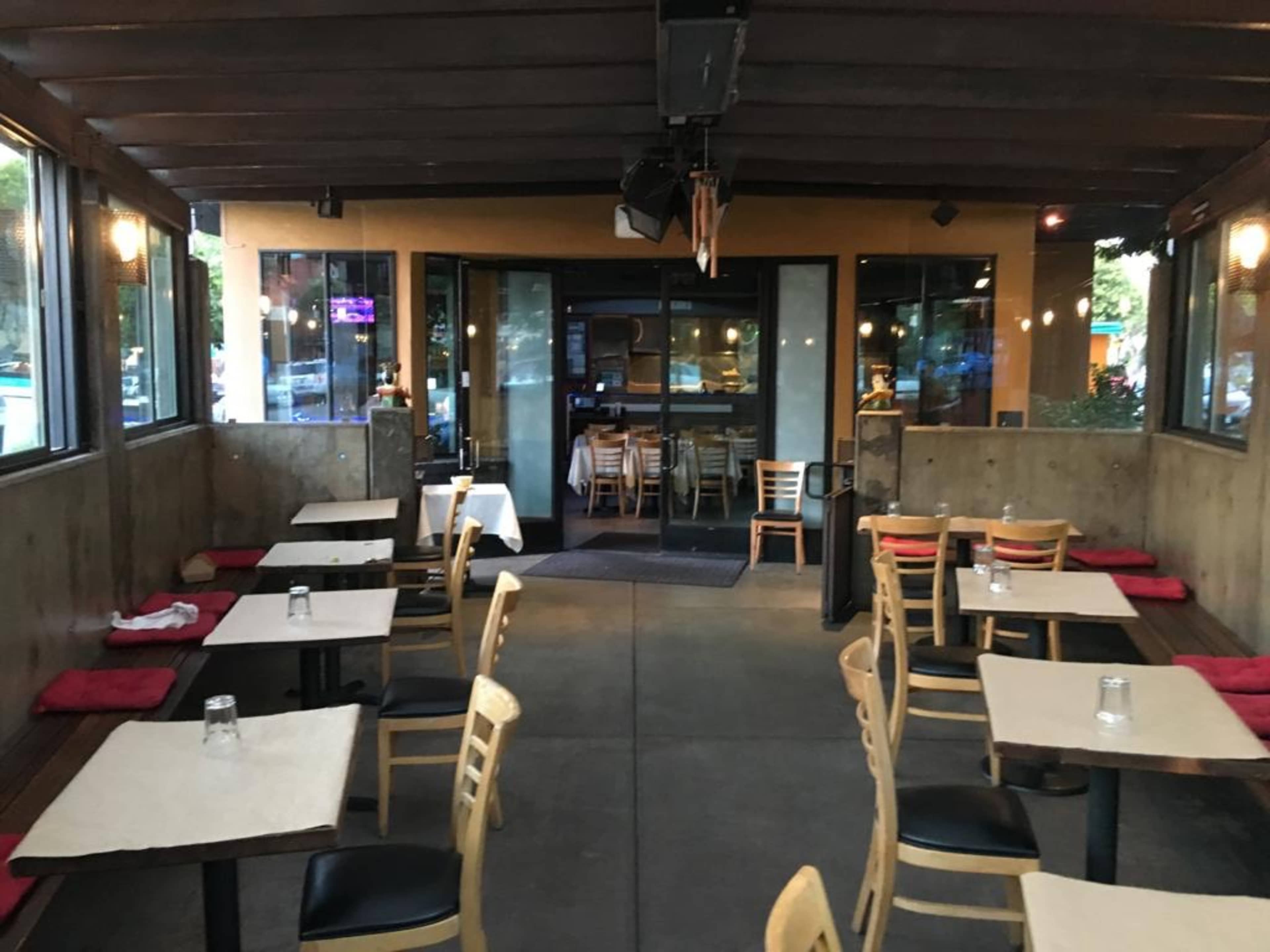 An empty restaurant interior with wooden tables and chairs arranged neatly in a dimly lit space.