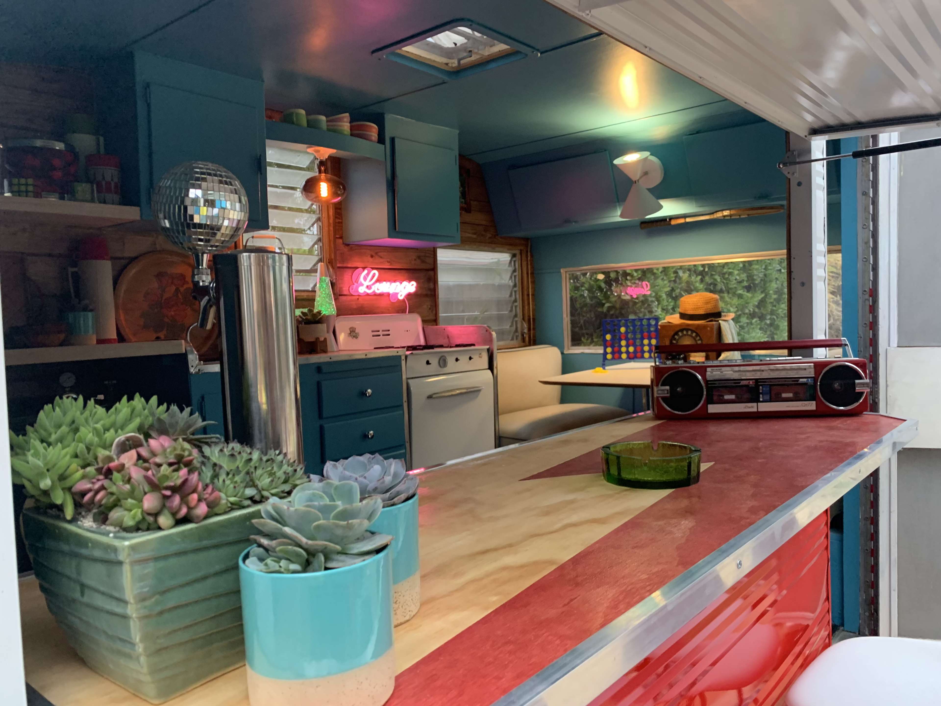 A colorful retro kitchen interior of a camper, featuring a disco ball, potted succulents, and vintage appliances.