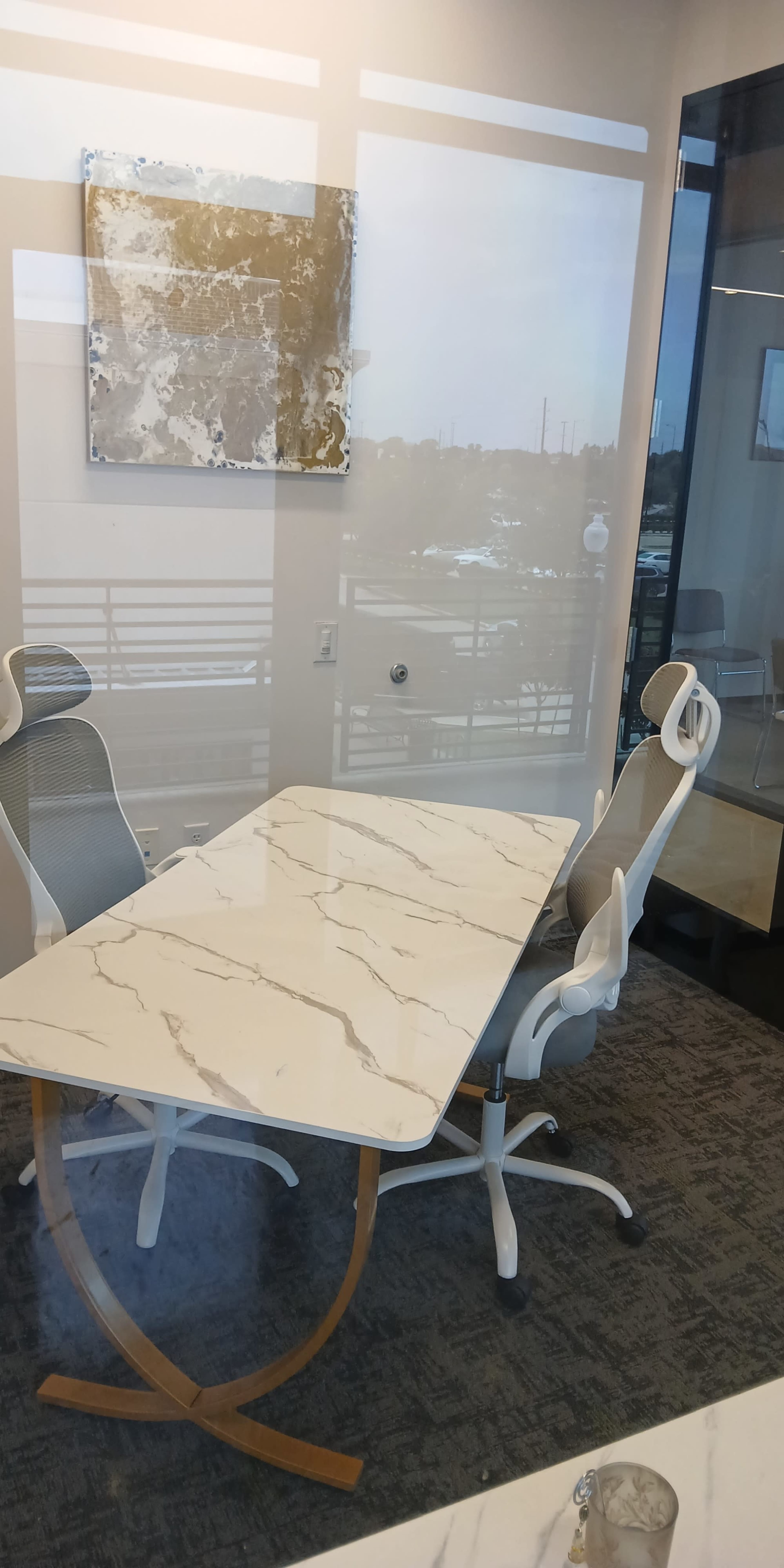 The image shows a modern conference room featuring a marble-top table with two white office chairs and a large window revealing an outdoor view.