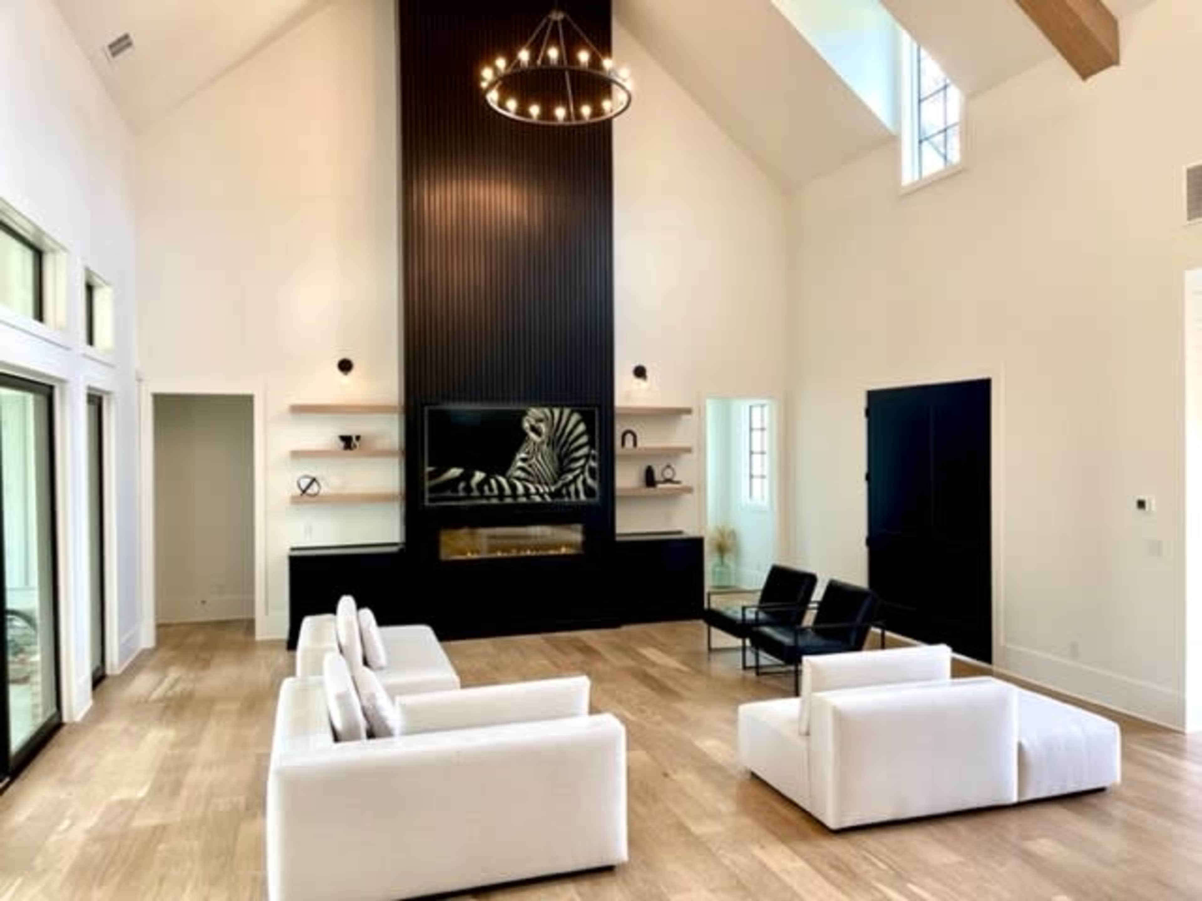 A spacious living room with two white sofas, a black television mounted on a wall, and a decorative fireplace beneath a tall, dark feature wall.