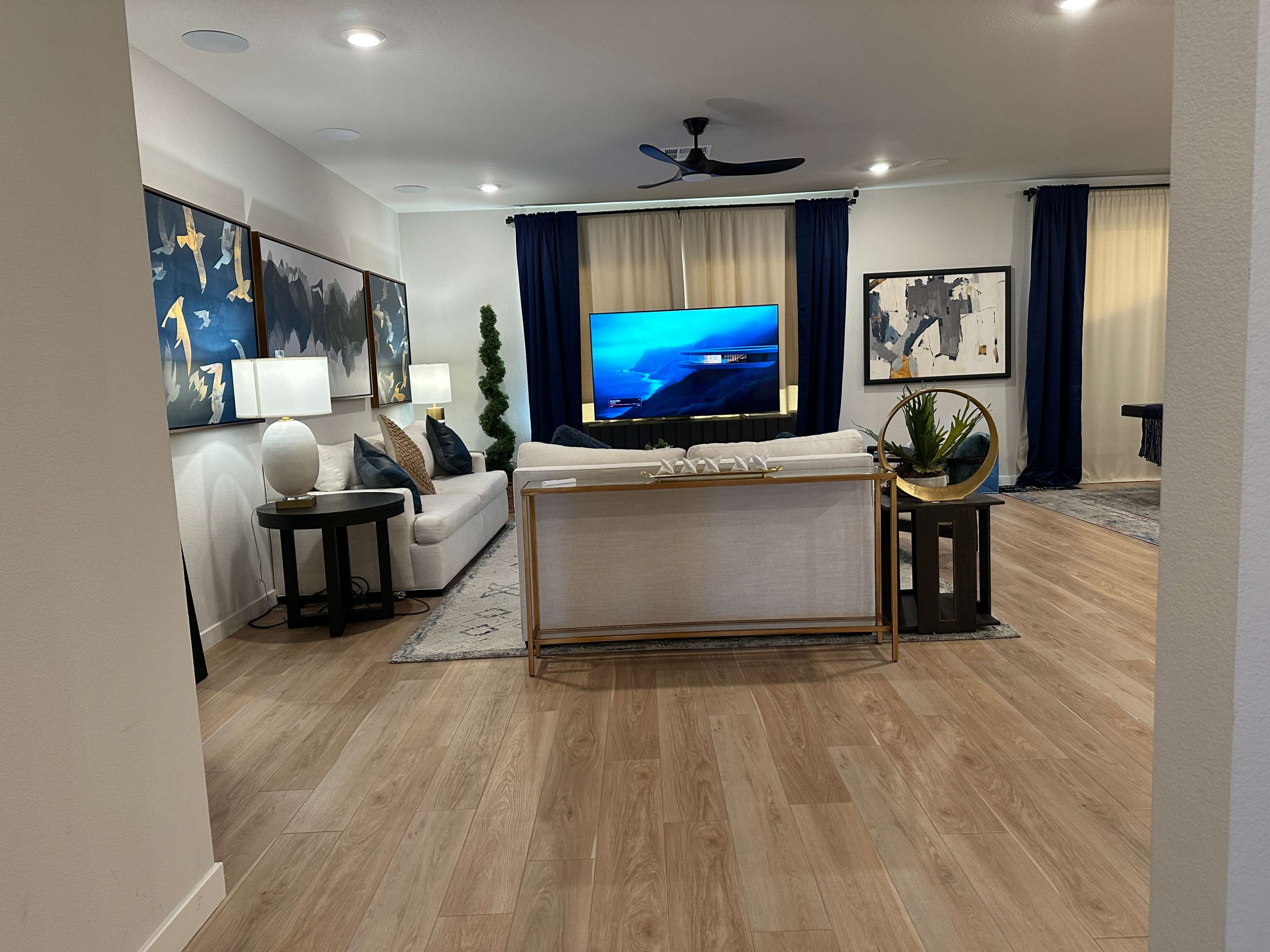 The image shows a modern living room with a white sofa, dark blue curtains, a large television, and decorative artwork on the walls.