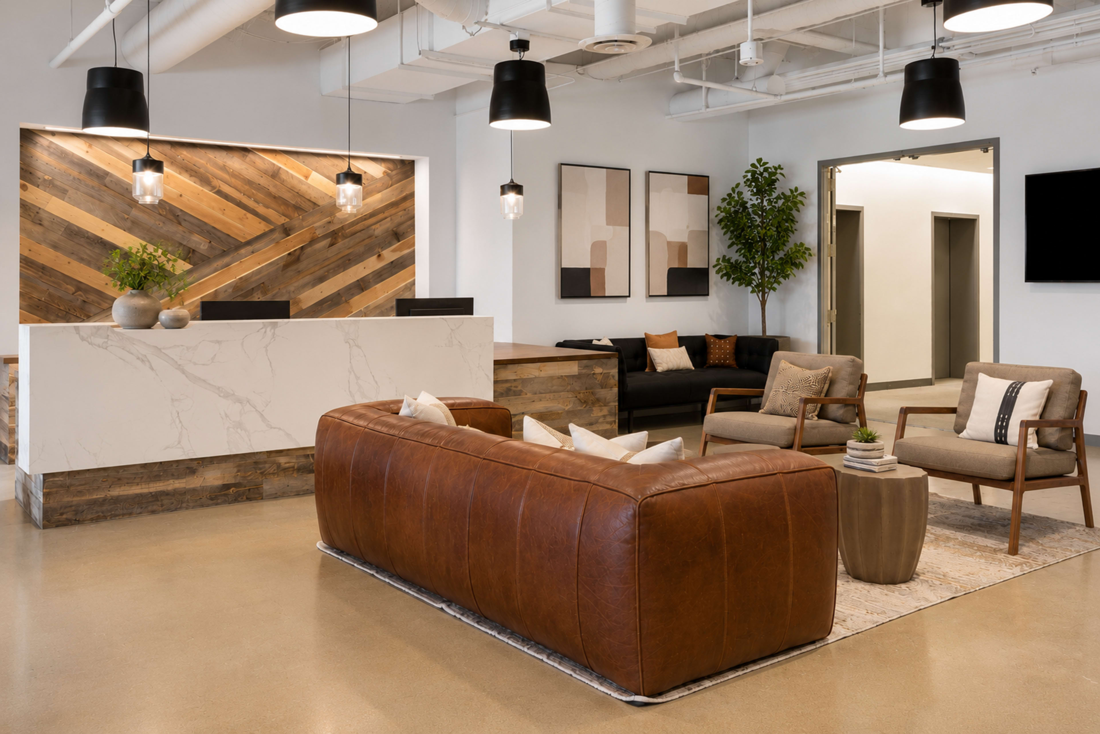 The image depicts a modern reception area featuring a brown leather couch, two armchairs, a geometric-patterned rug, and a wooden reception desk with accent lighting.