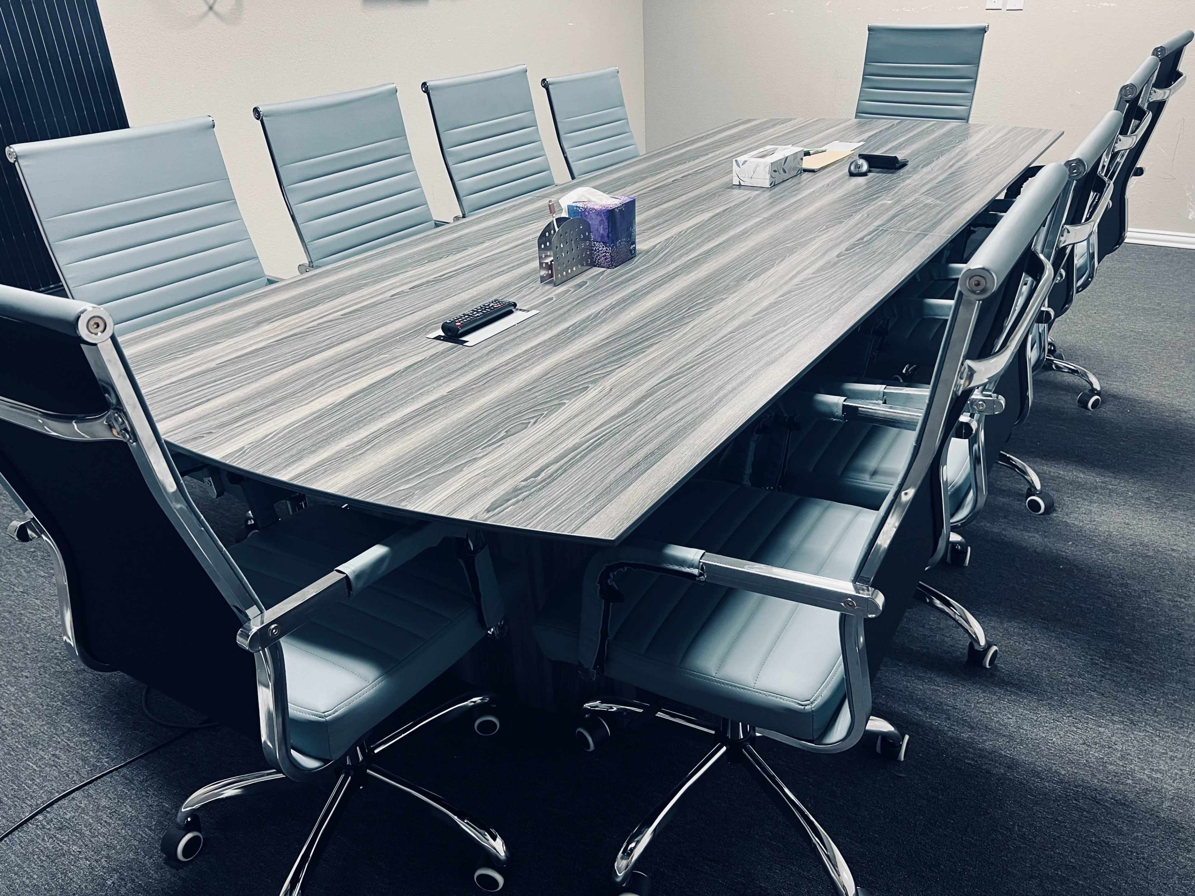 A long, oval conference table surrounded by ten light blue office chairs is set up in a meeting room.