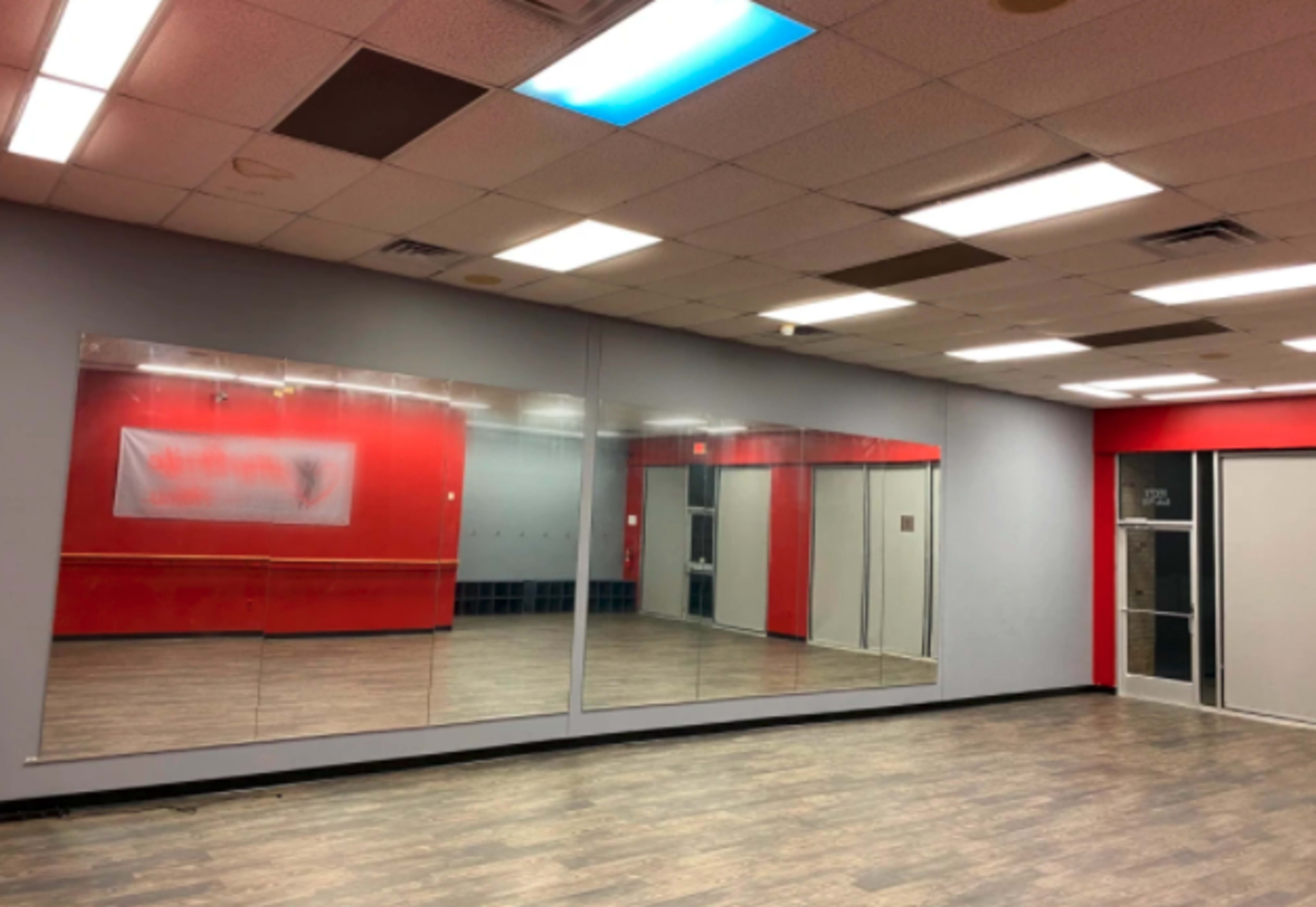 A spacious dance studio featuring large mirrors on one wall and red and gray walls.