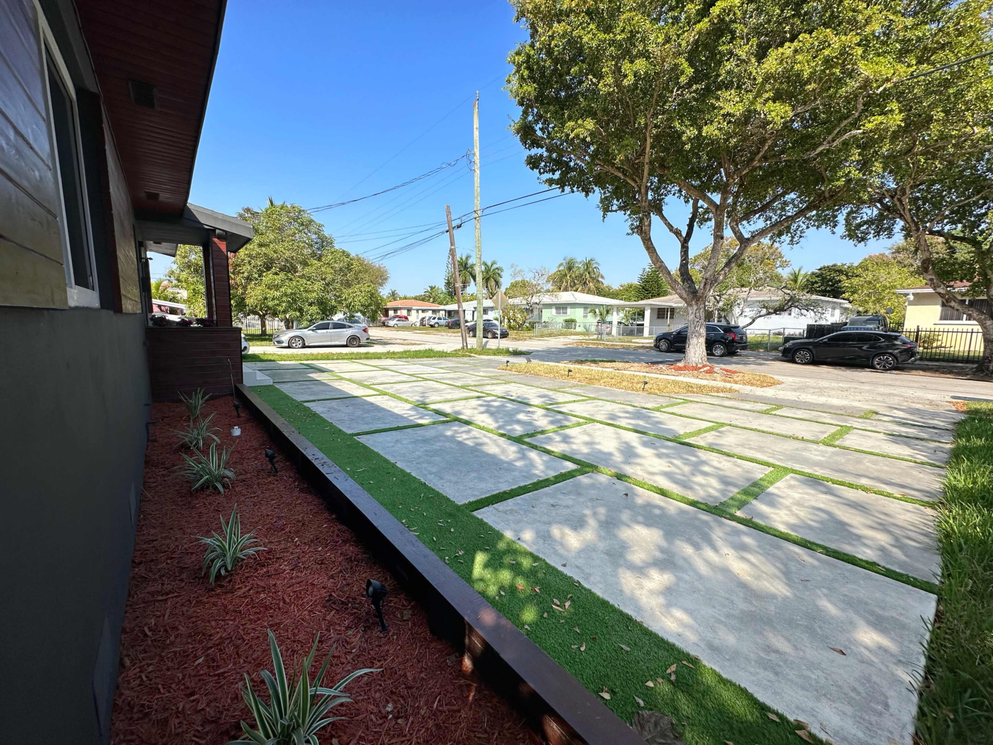 A rectangular concrete driveway bordered by grassy patches and surrounded by trees, with a clear view of a residential street.