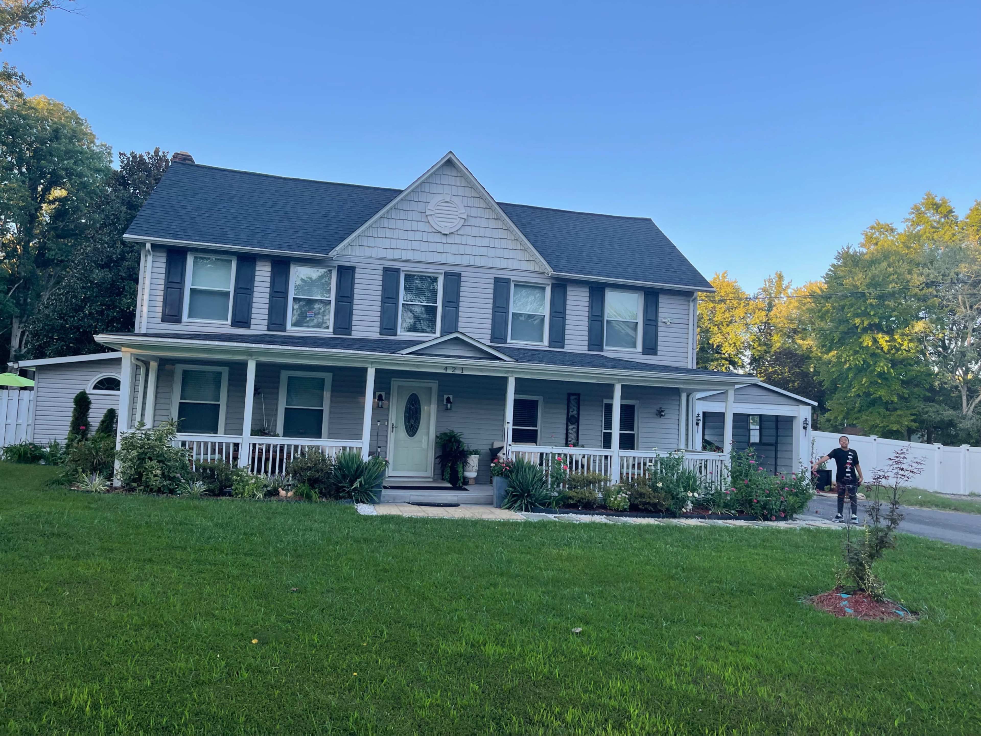 A two-story house with a gray exterior, dark shutters, and a front porch is set on a grassy lawn.