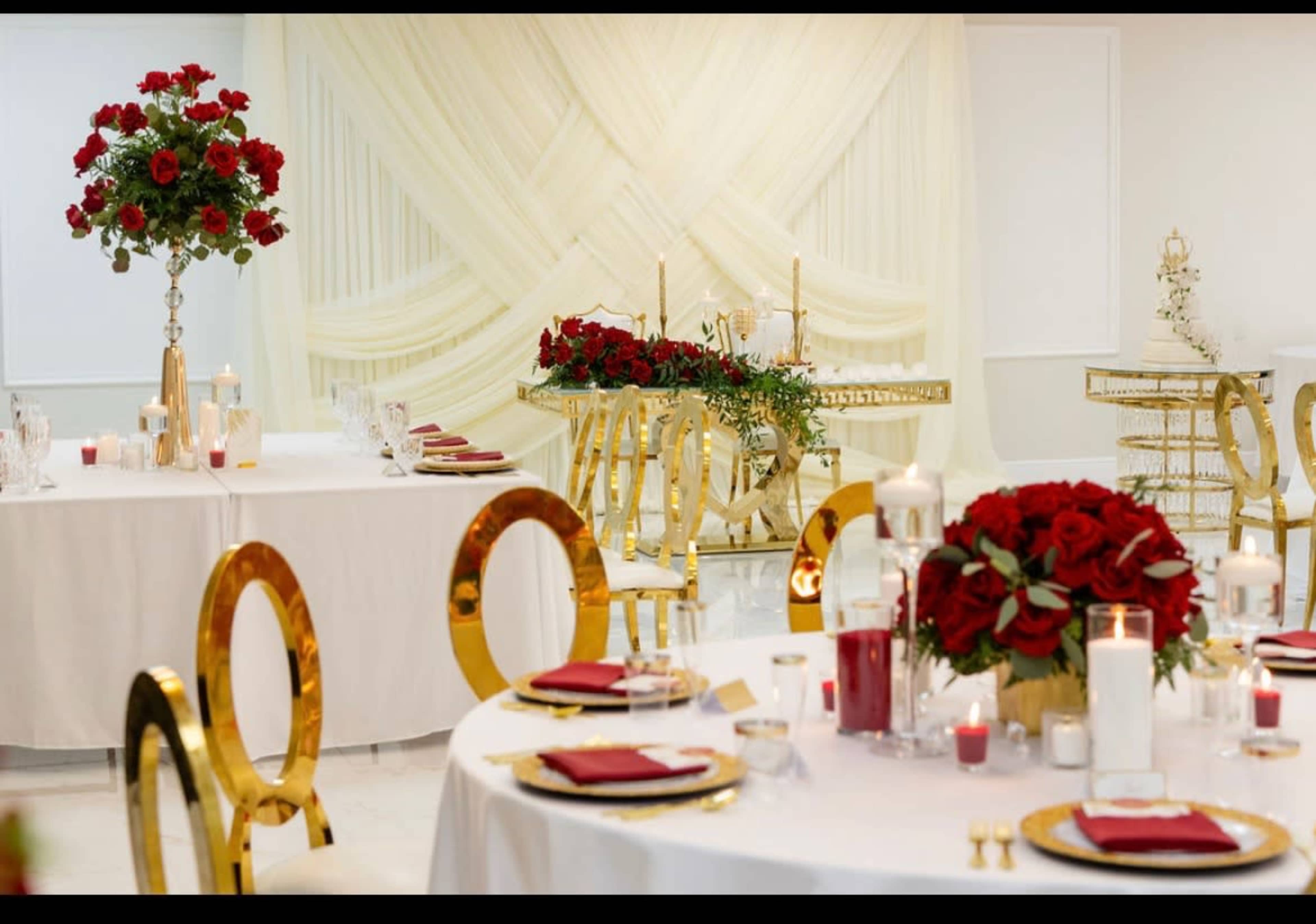 The image shows elegantly arranged tables with white tablecloths, gold accents, and centerpieces of red roses in a luxurious event space.