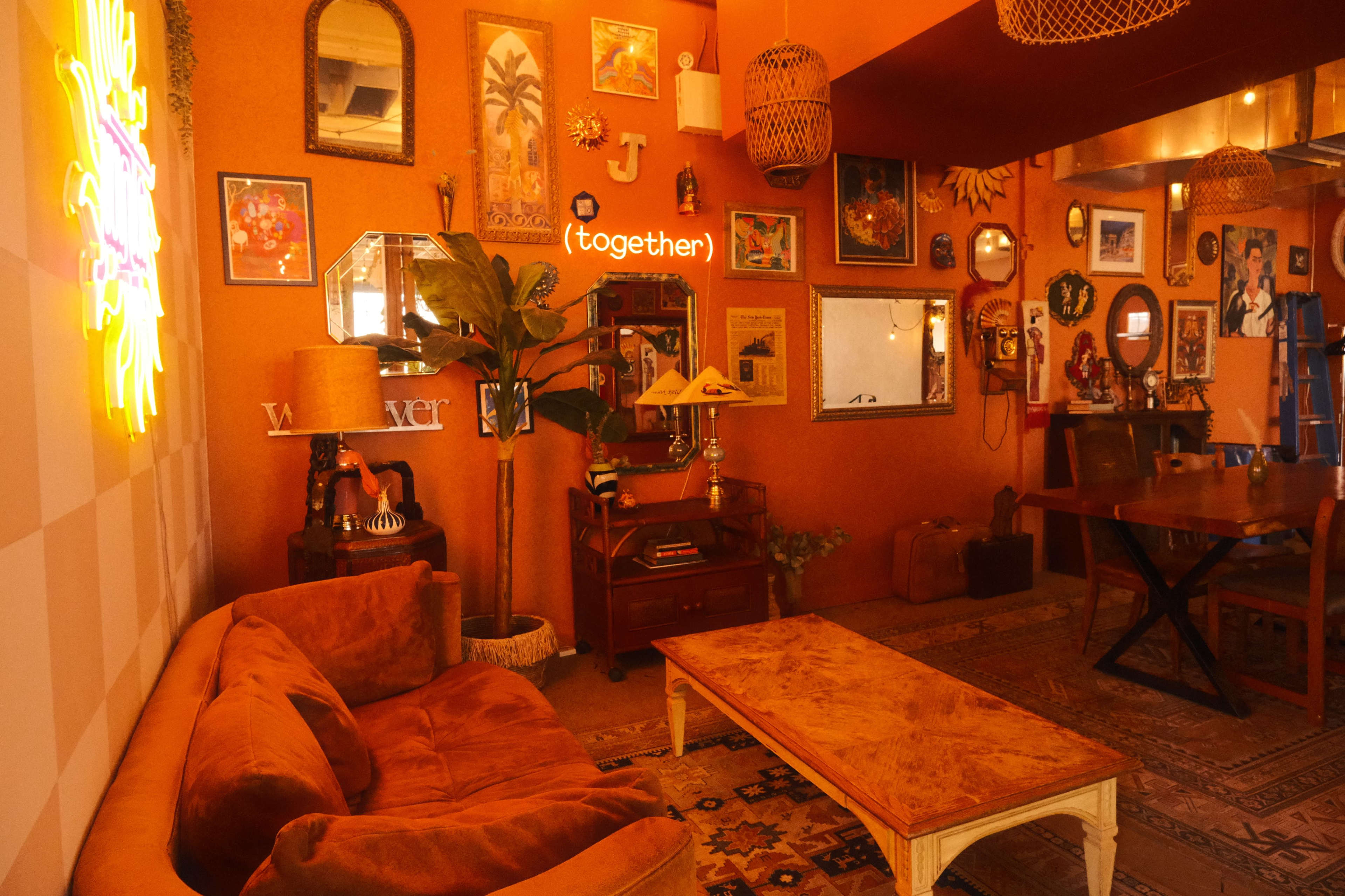 A cozy, orange-toned living area features a plush couch, a wooden coffee table, framed artwork on the walls, and decorative plants.