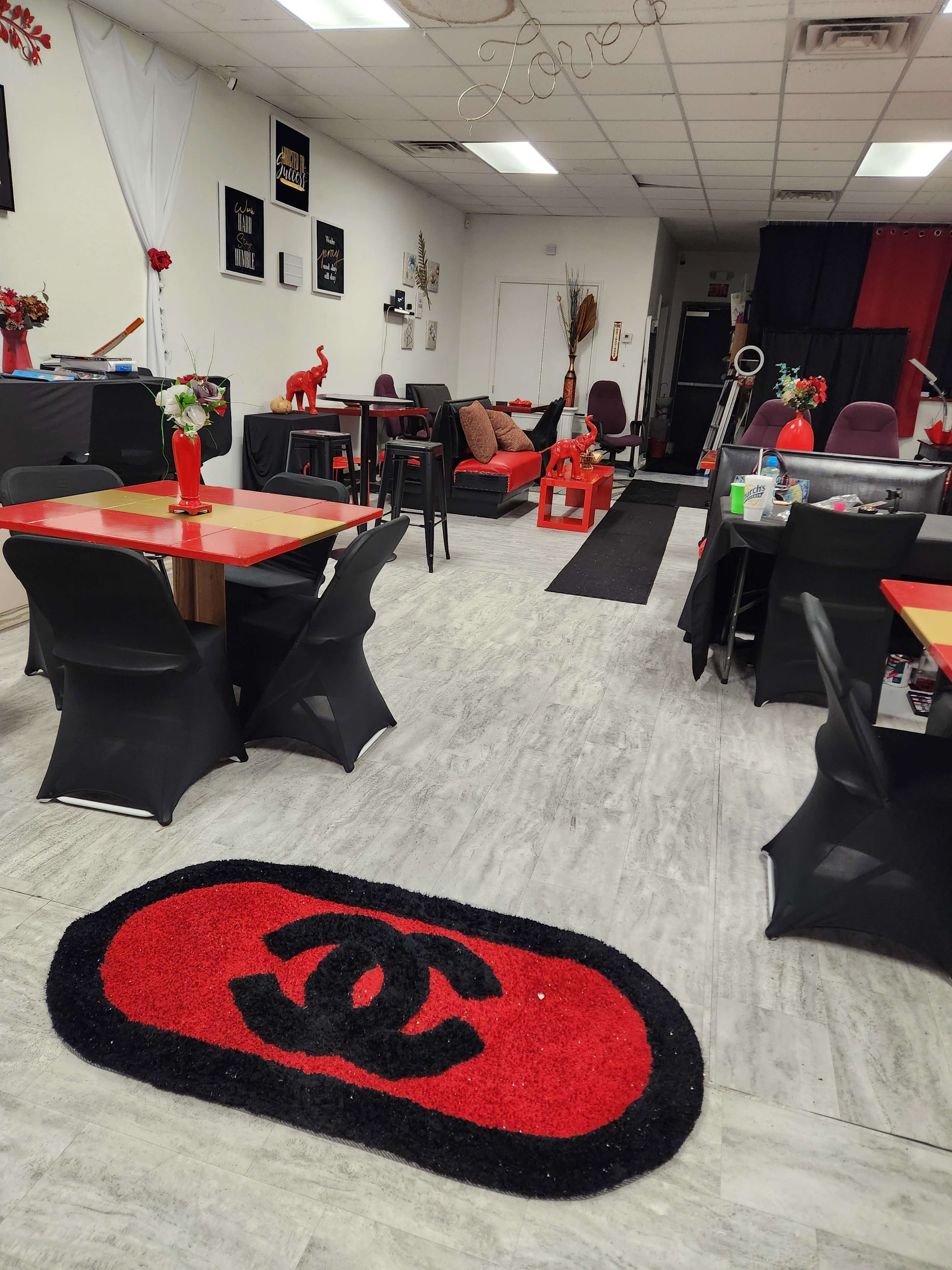 A bright interior of a cafe or small dining area with red and black decor, including tables, chairs, and a Chanel logo mat at the entrance.