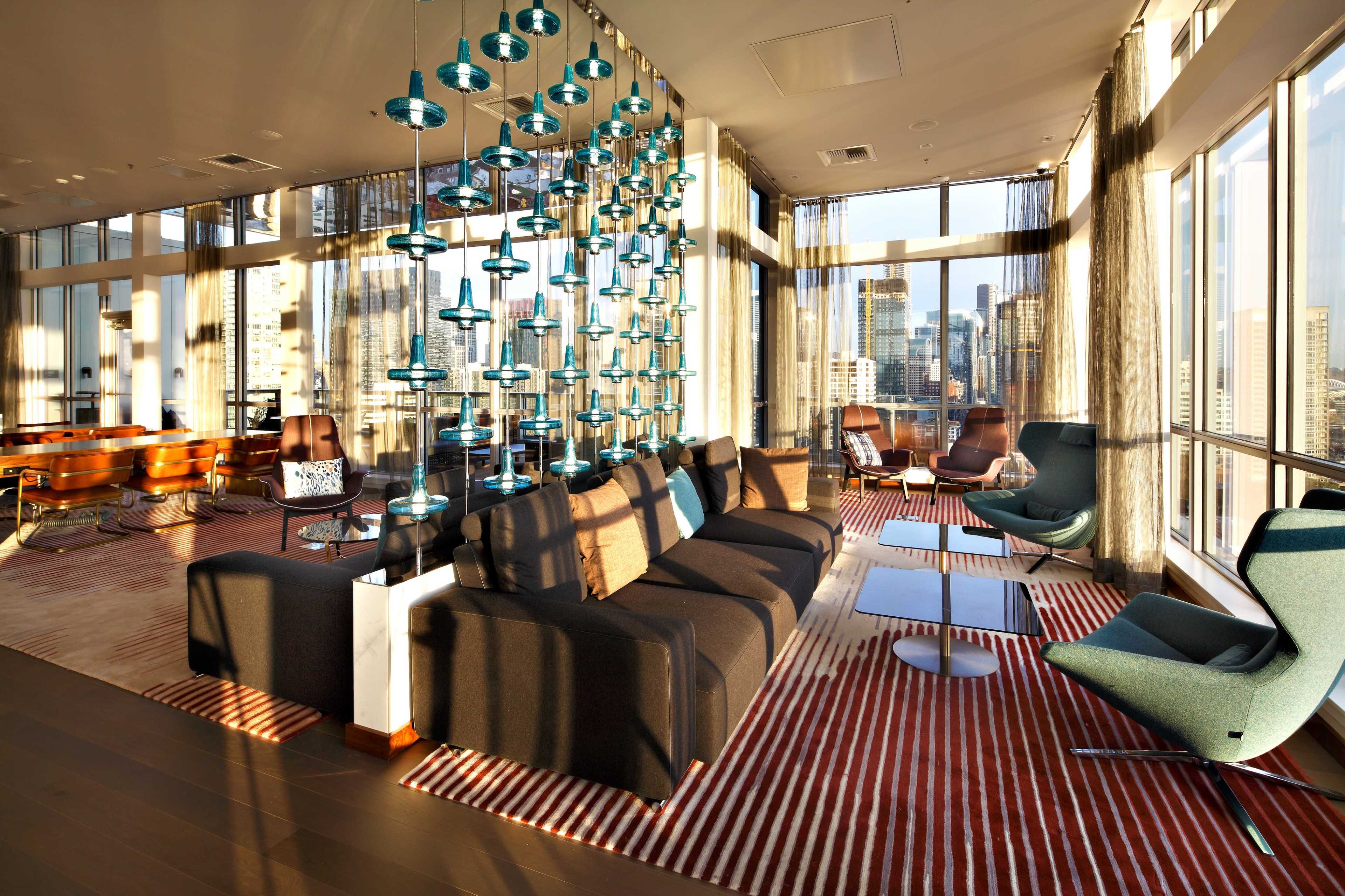 A modern living space with large windows offering a view of the city, featuring a sectional sofa, stylish chairs, and a unique light installation.
