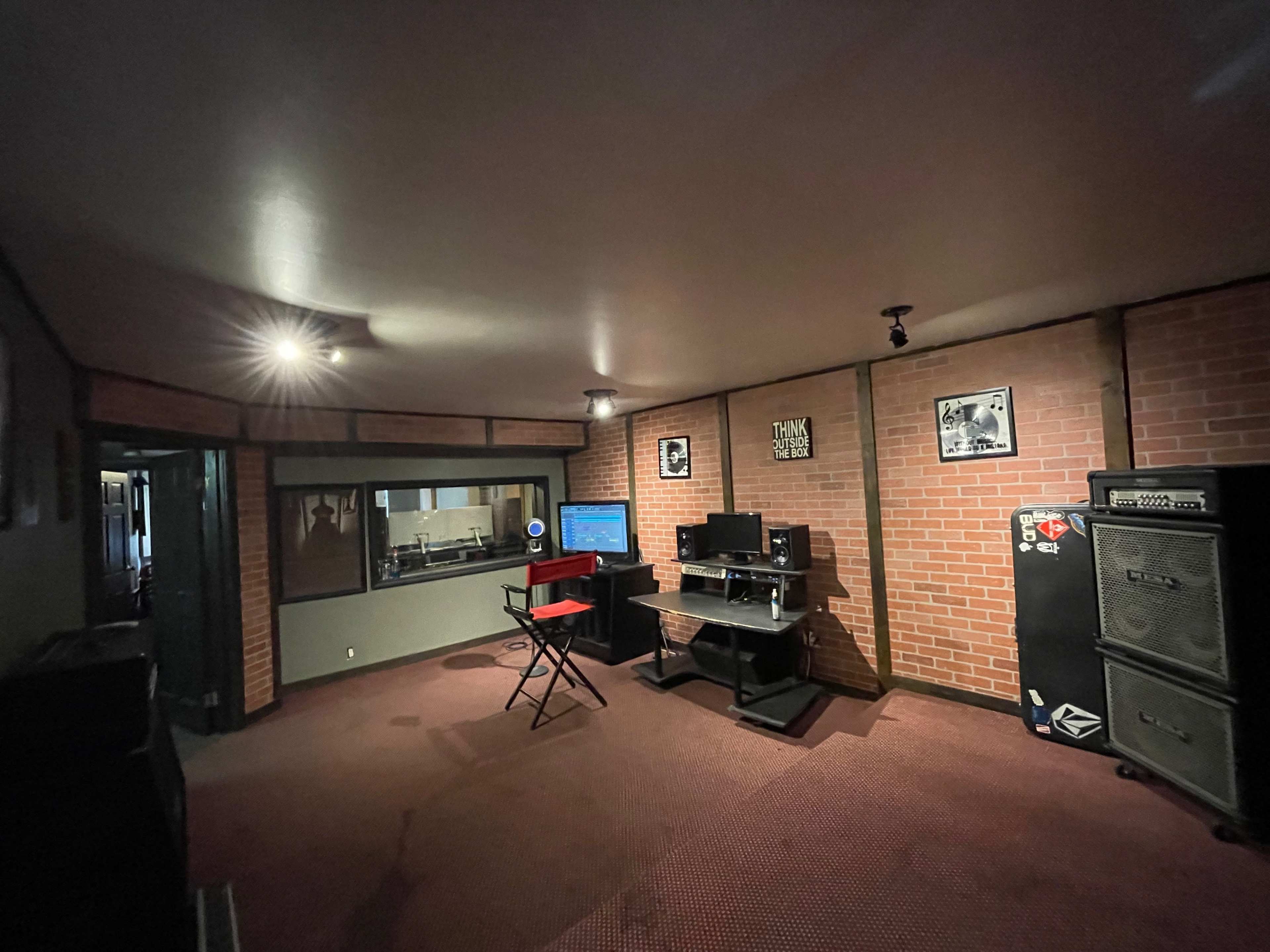 A studio room with brick walls, a desk with computer equipment, and an amplifier in the corner.