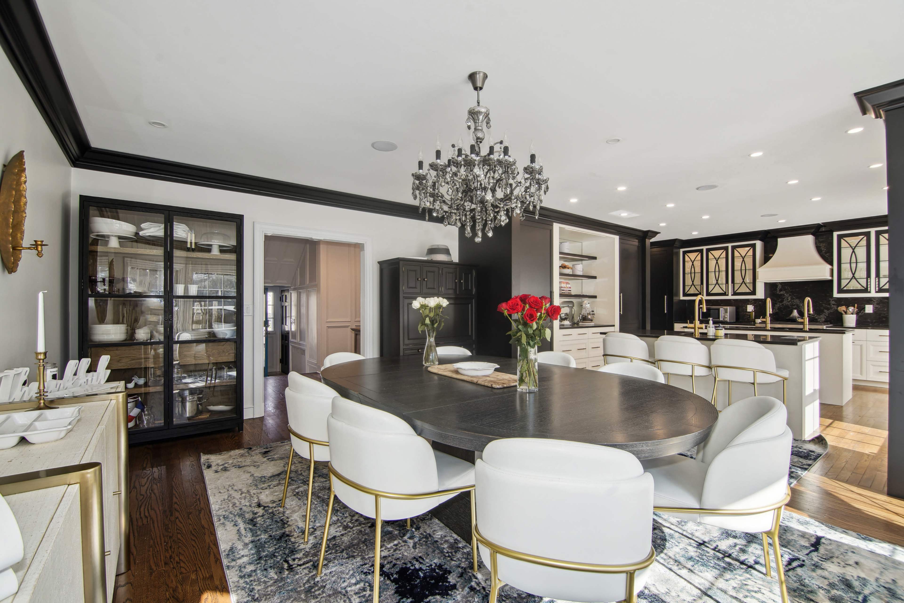 A modern dining room featuring a large round table surrounded by white chairs, with a chandelier hanging above and a black and white color scheme.