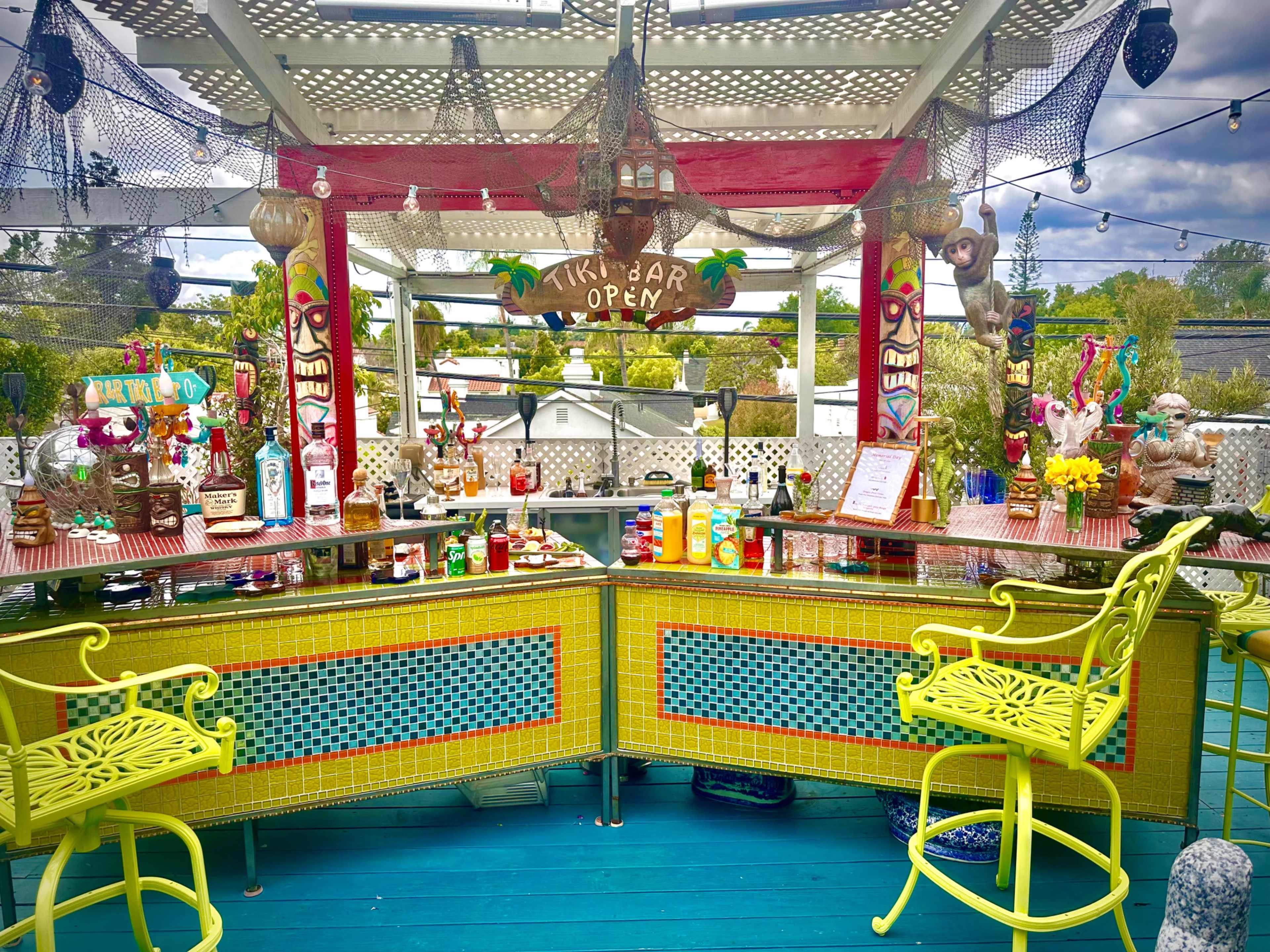 A brightly colored tiki bar with an array of liquor bottles, decorations, and seating under a covered outdoor area.