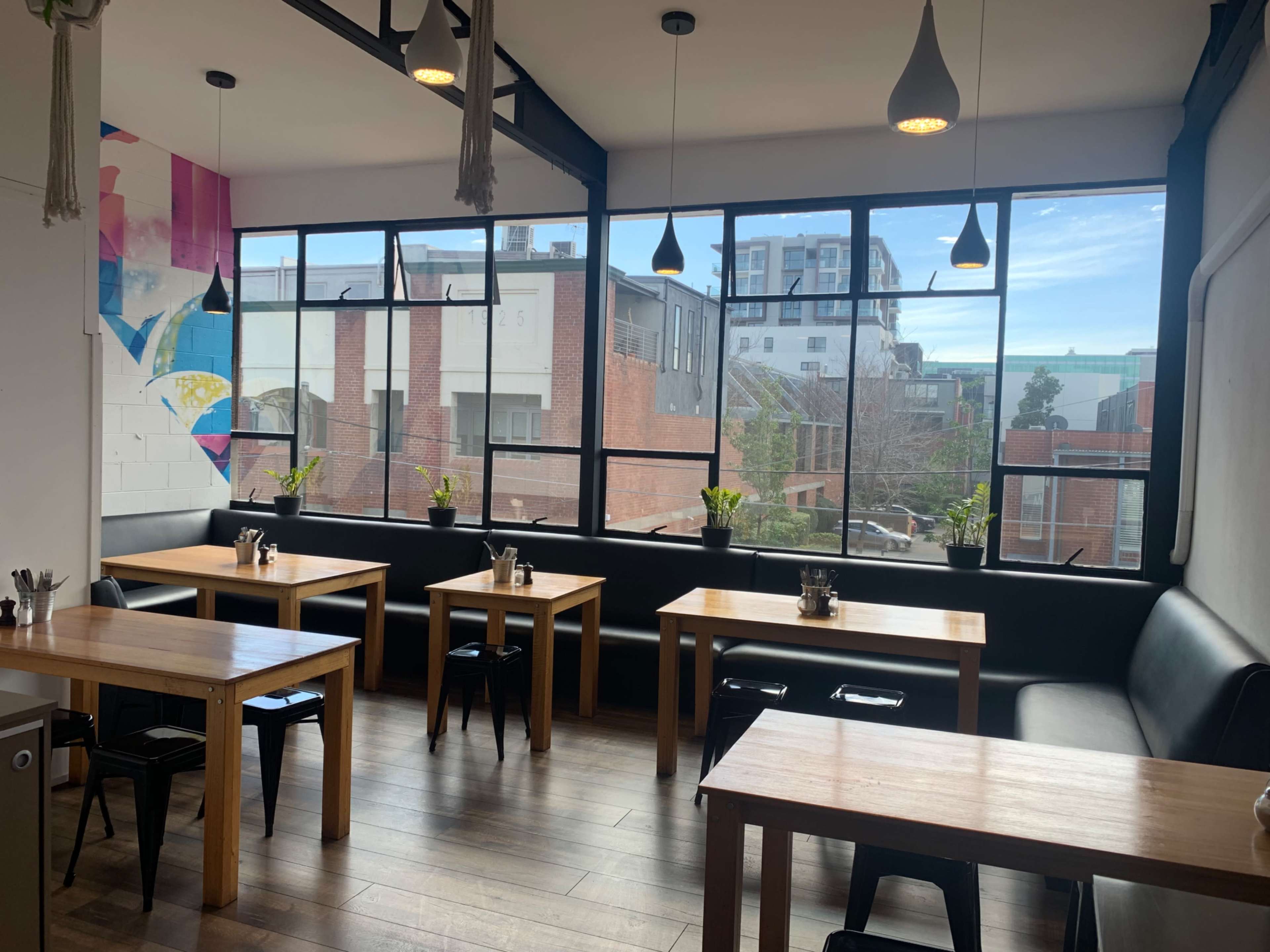 A modern cafe interior with wooden tables, black chairs, and large windows overlooking a cityscape.