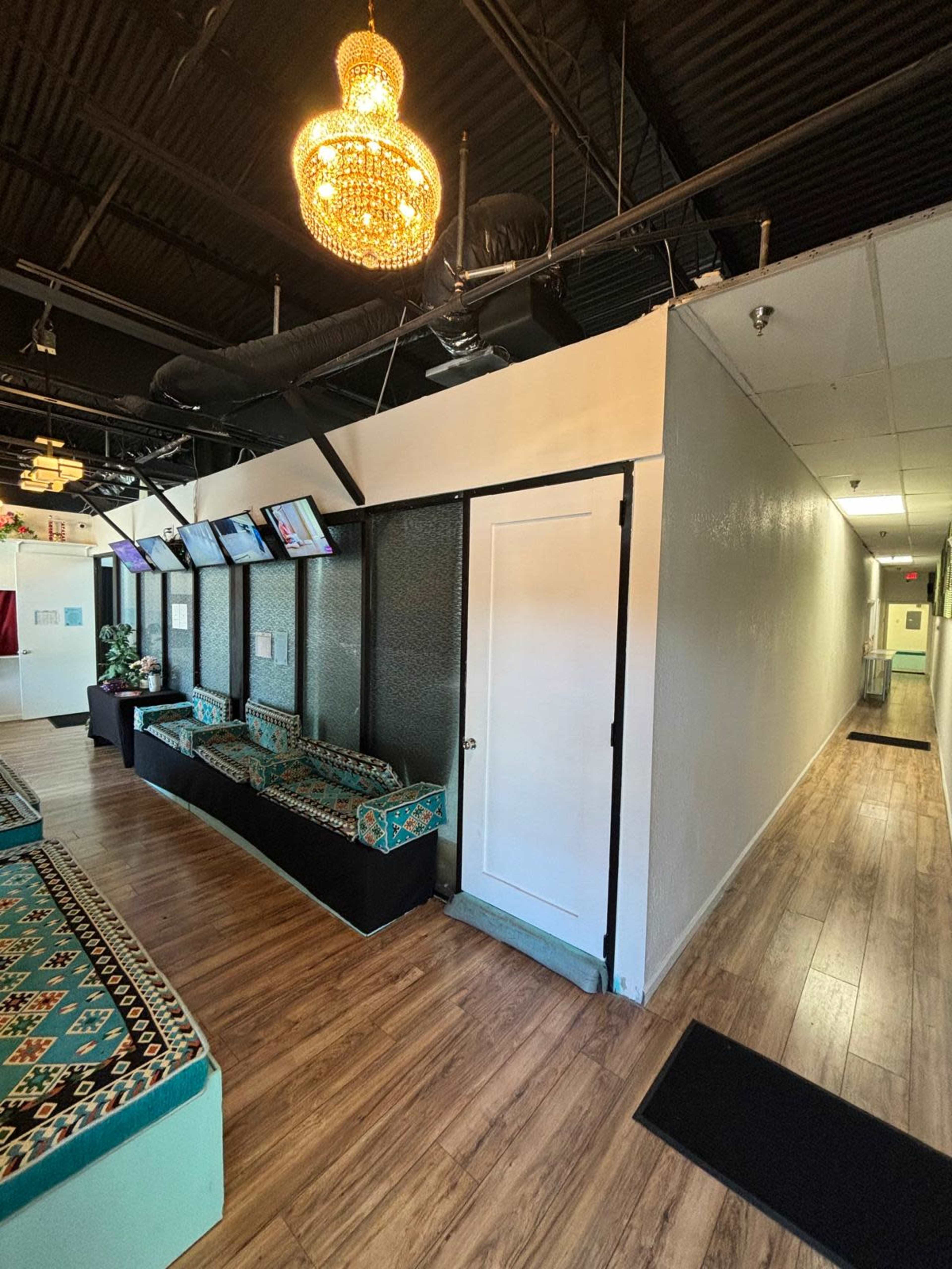 The image depicts a spacious interior with a seating area featuring patterned couches, a chandelier, and a long hallway leading to additional rooms.