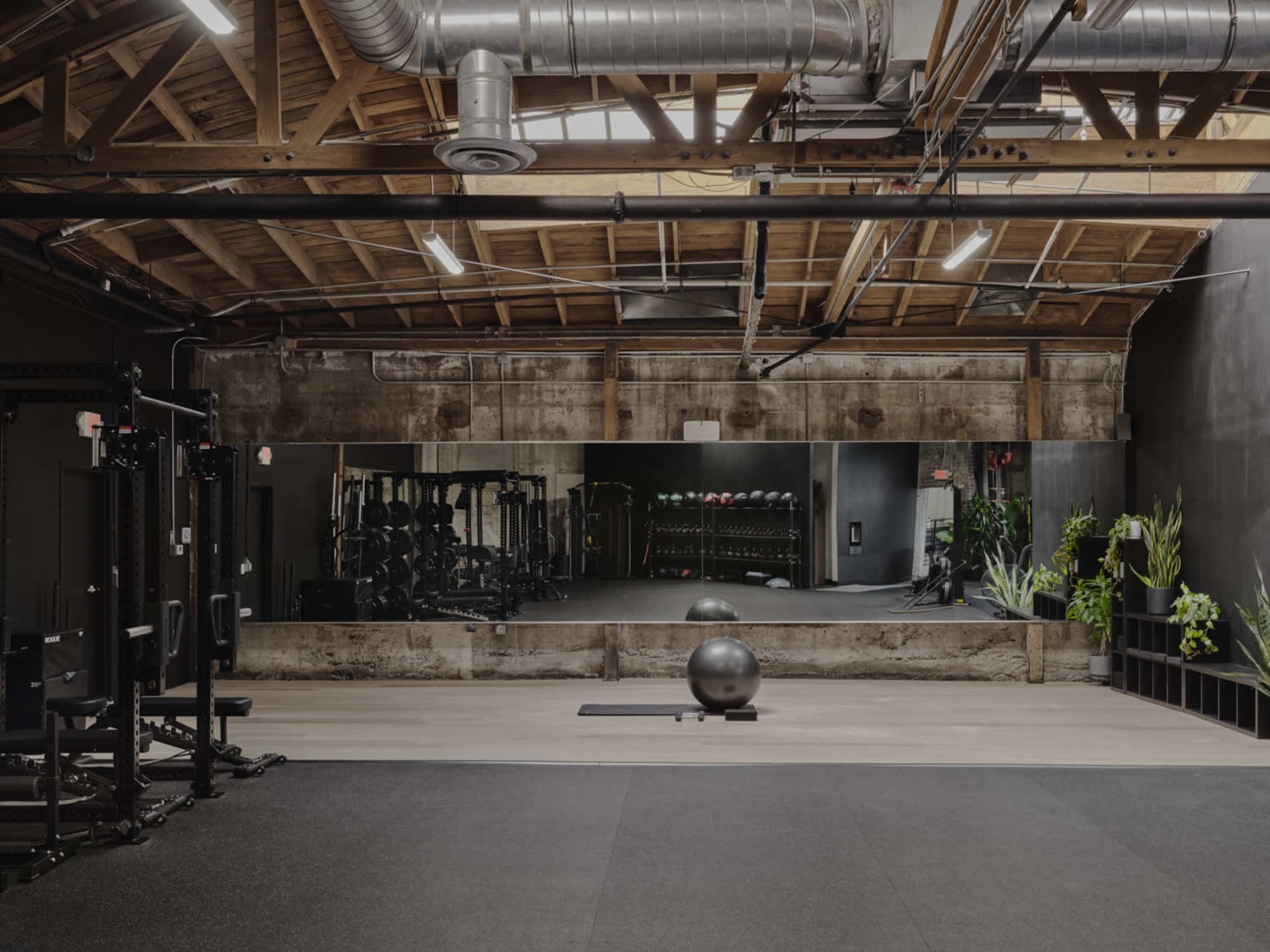 A spacious gym with a mirrored wall, fitness equipment, and a large exercise ball placed on the floor.