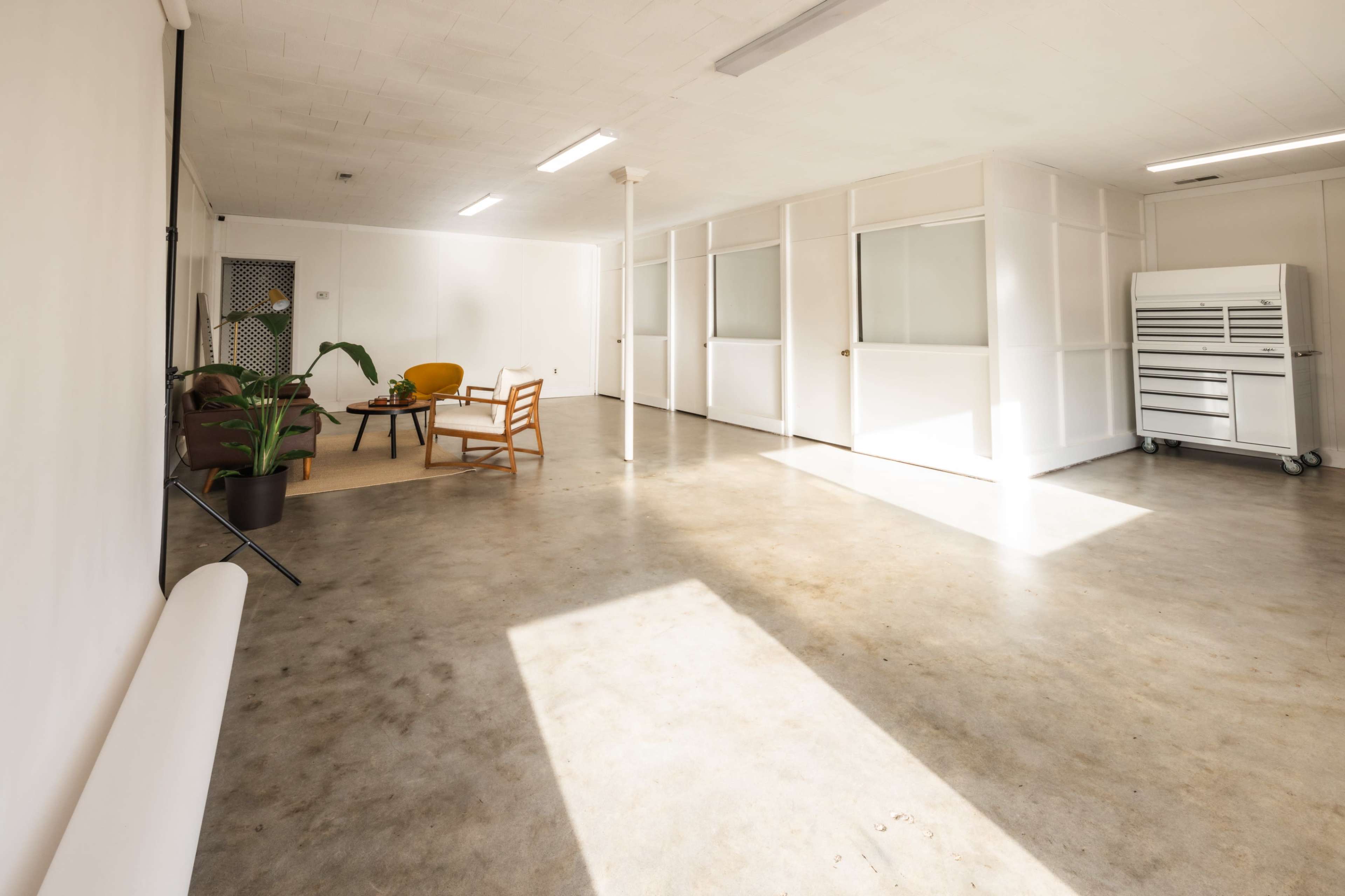 A spacious, well-lit room with concrete flooring, featuring a seating area with a chair and small table, along with storage cabinets in the background.