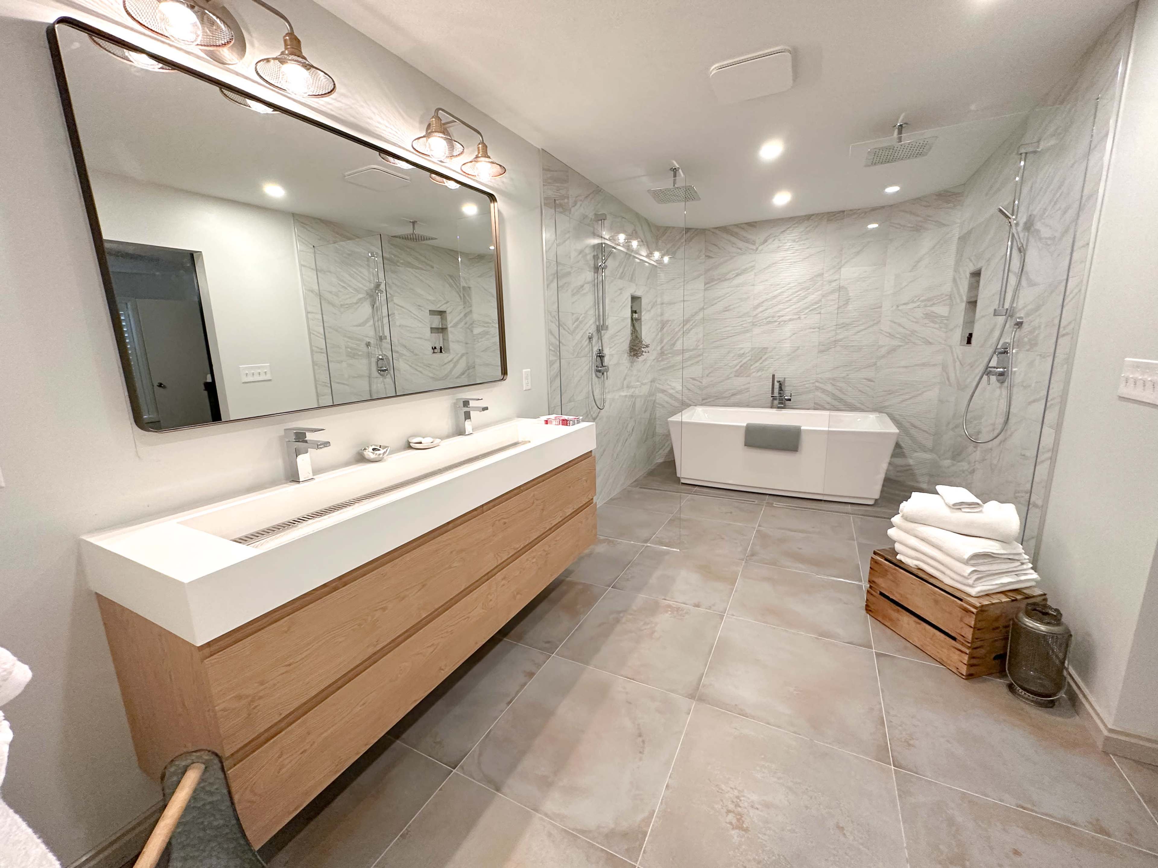 A modern bathroom featuring a freestanding tub, a double vanity with a large mirror, and gray marble walls.