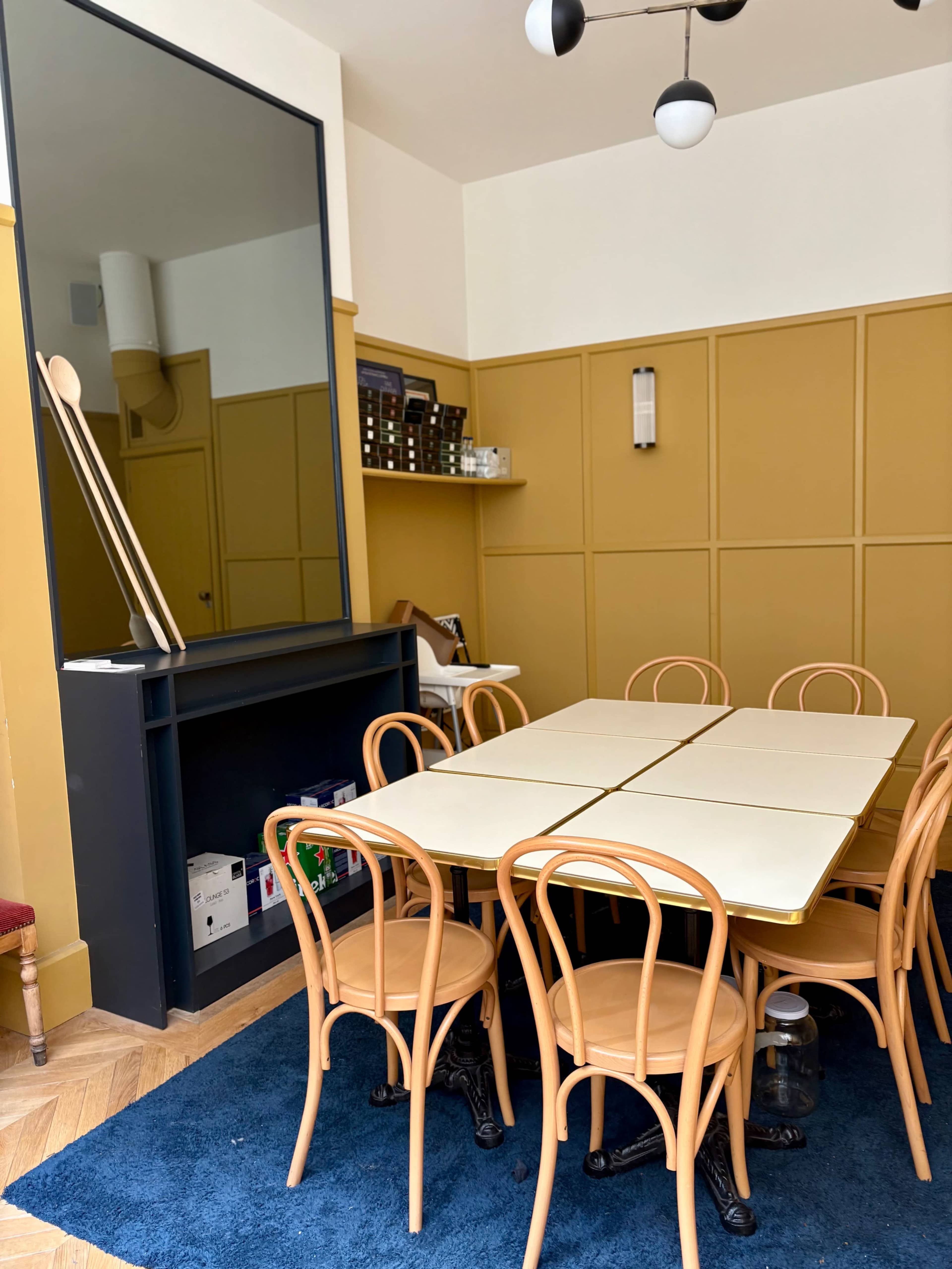 A spacious dining area features a large table surrounded by bentwood chairs, with a mirror and a dark cabinet on the wall.
