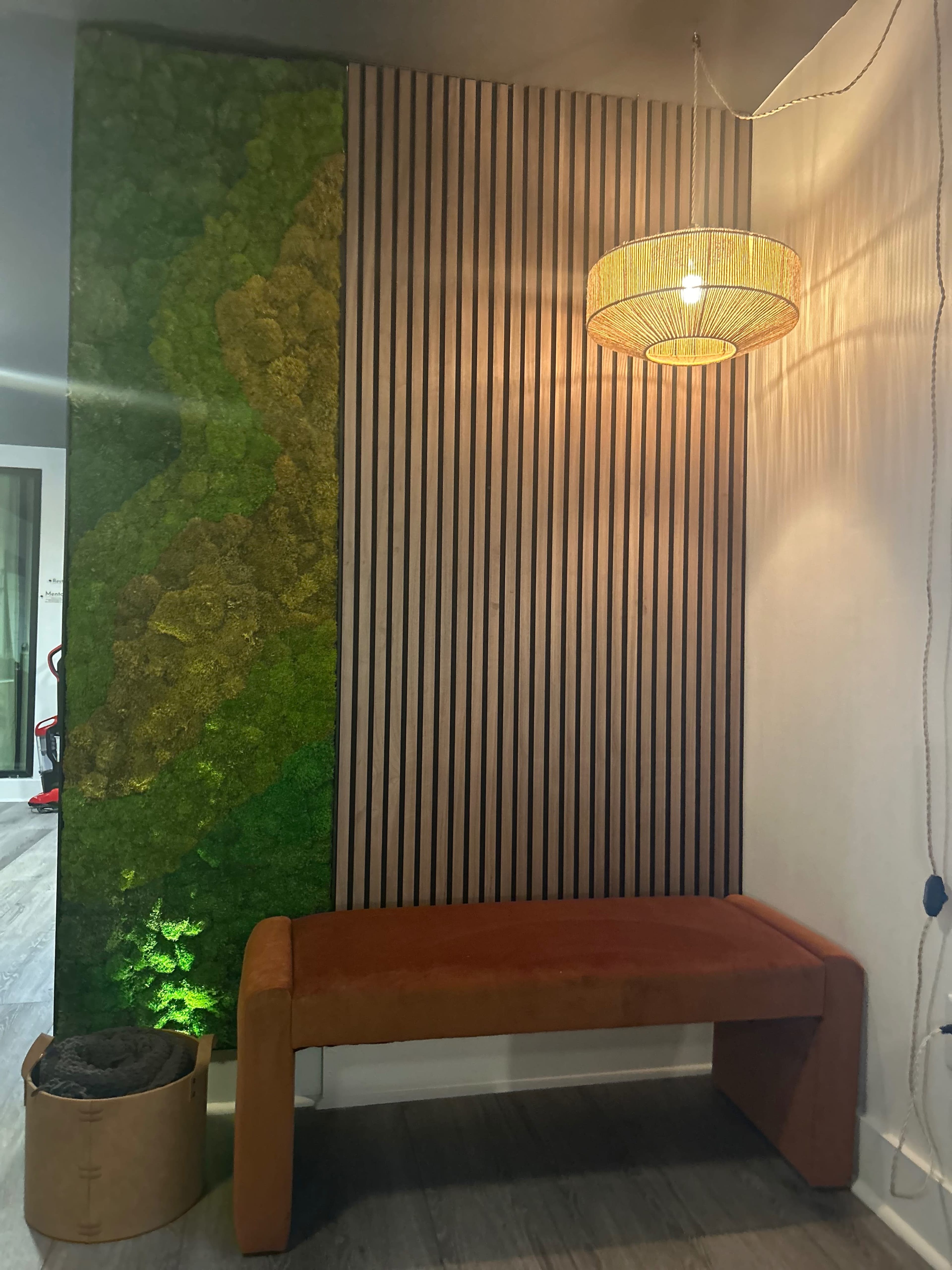 A modern interior with a green moss-covered wall, a wooden slatted wall, an orange bench, and a hanging light fixture.