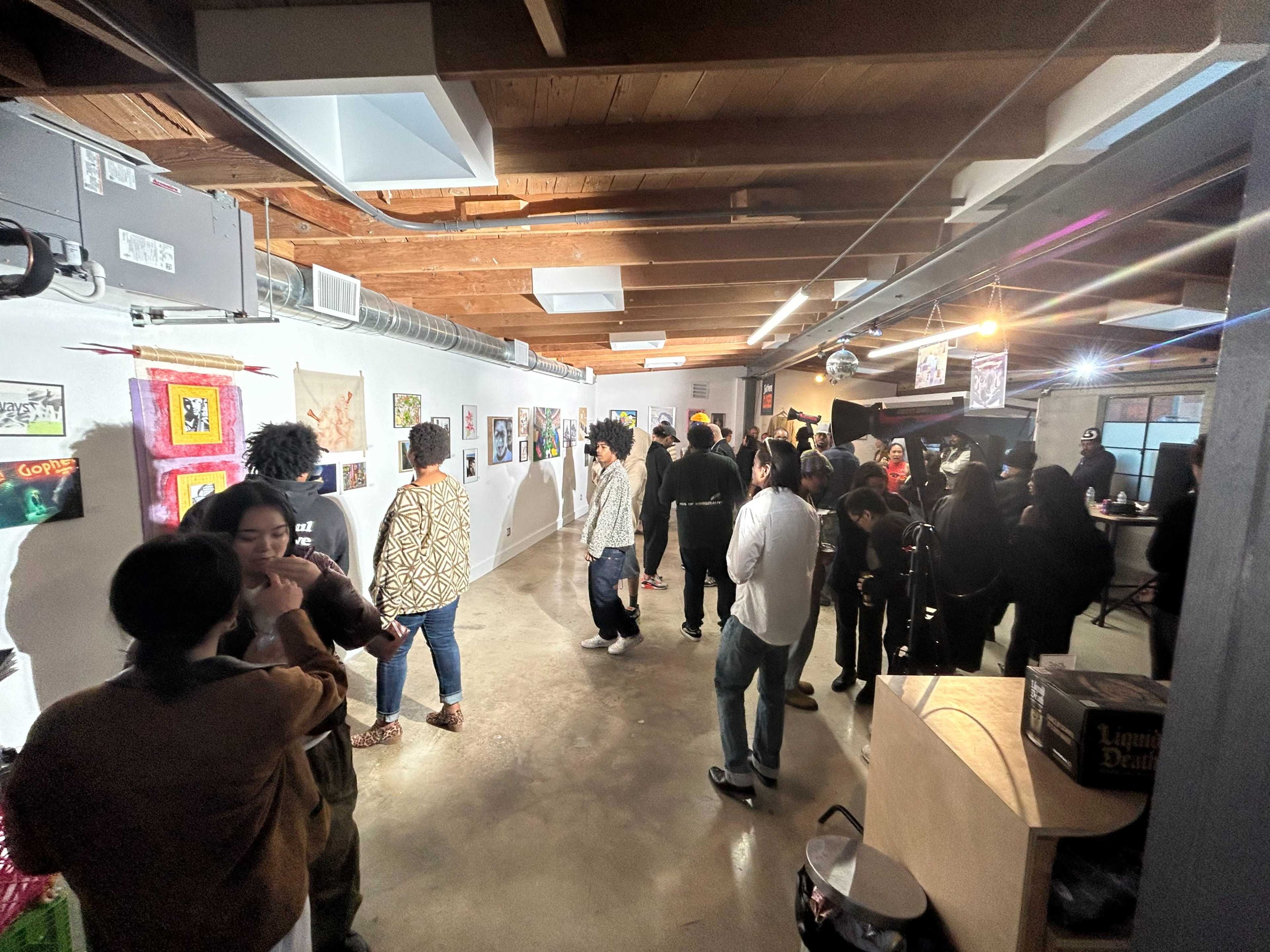 A group of people gather in a well-lit gallery space featuring various pieces of art displayed on the walls.