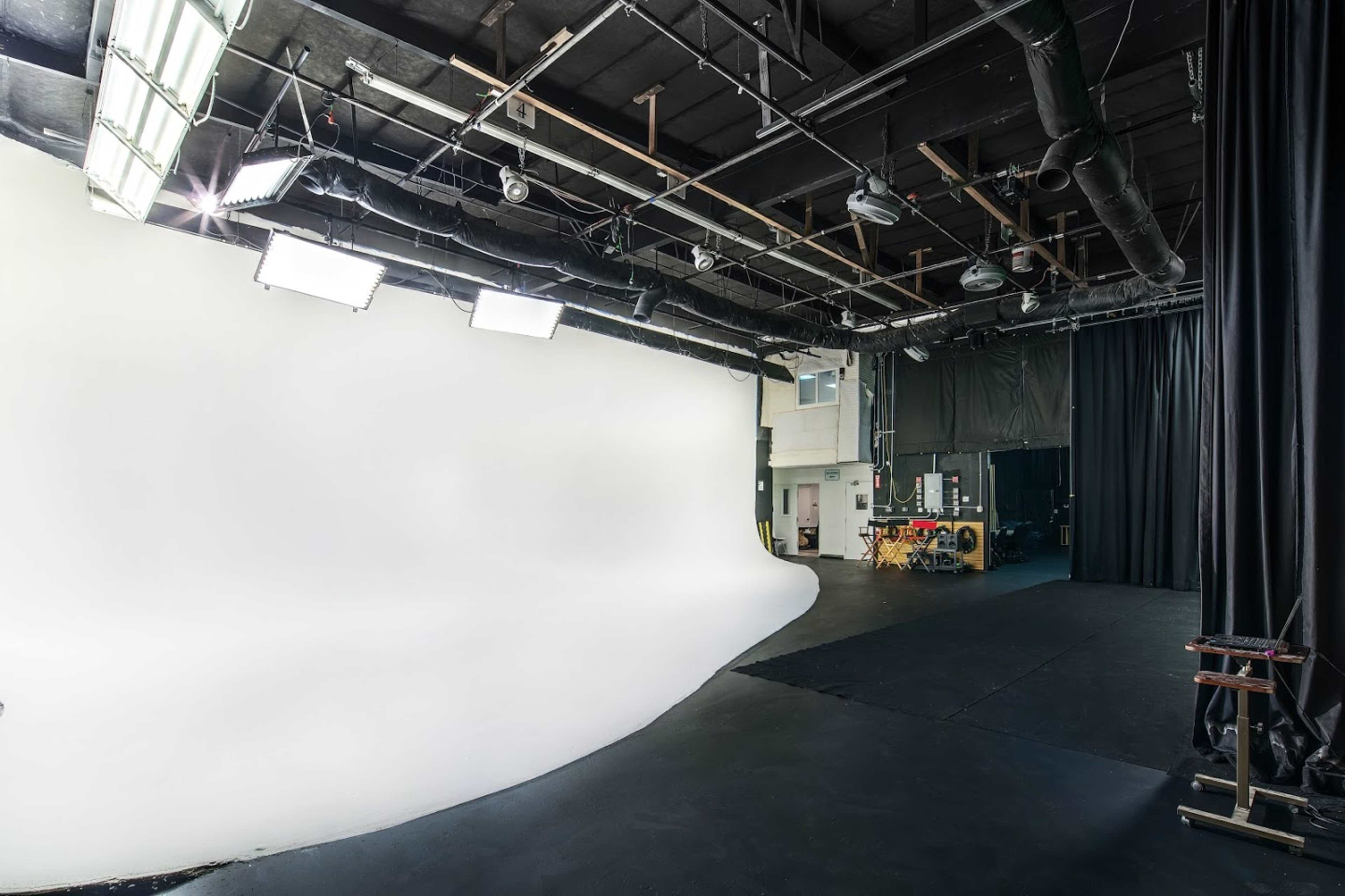 A spacious film studio with a curved white backdrop, overhead lighting, and equipment along the side.