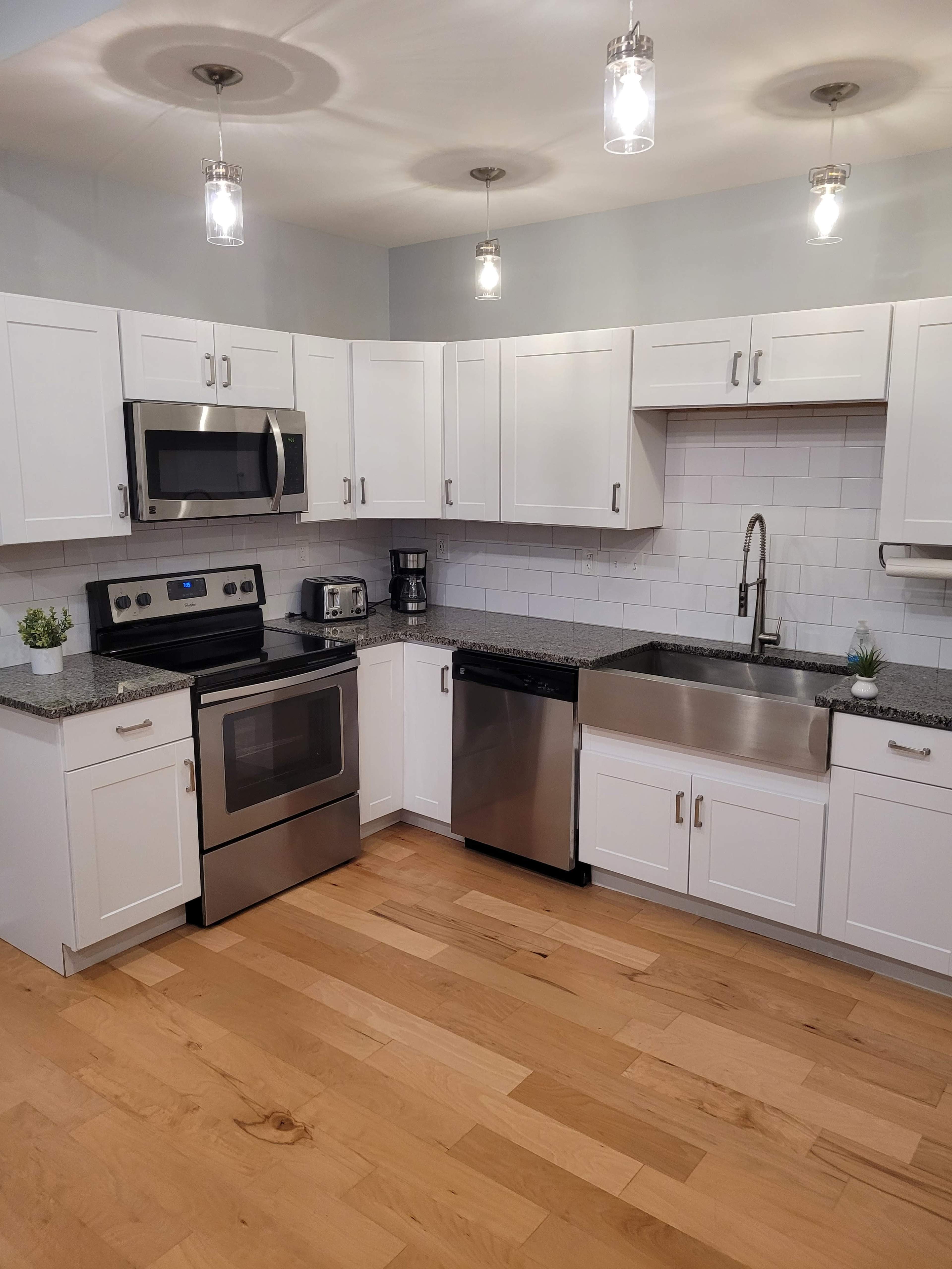 A modern kitchen with white cabinets, stainless steel appliances, and a large sink, featuring a light wood floor.