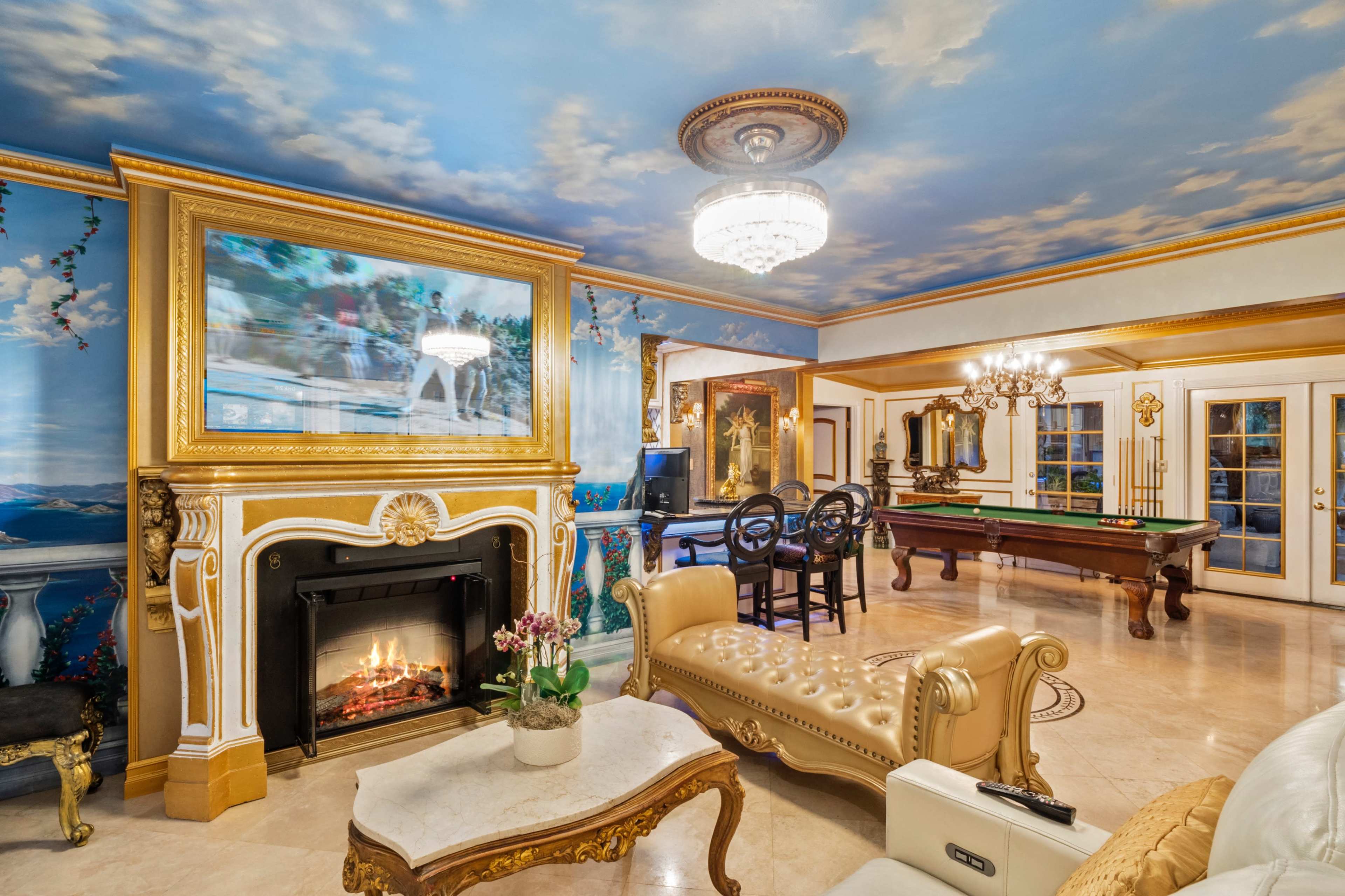 The interior features a lavish room with a fireplace, ornate furnishings, a billiards table, and a painted ceiling depicting clouds.
