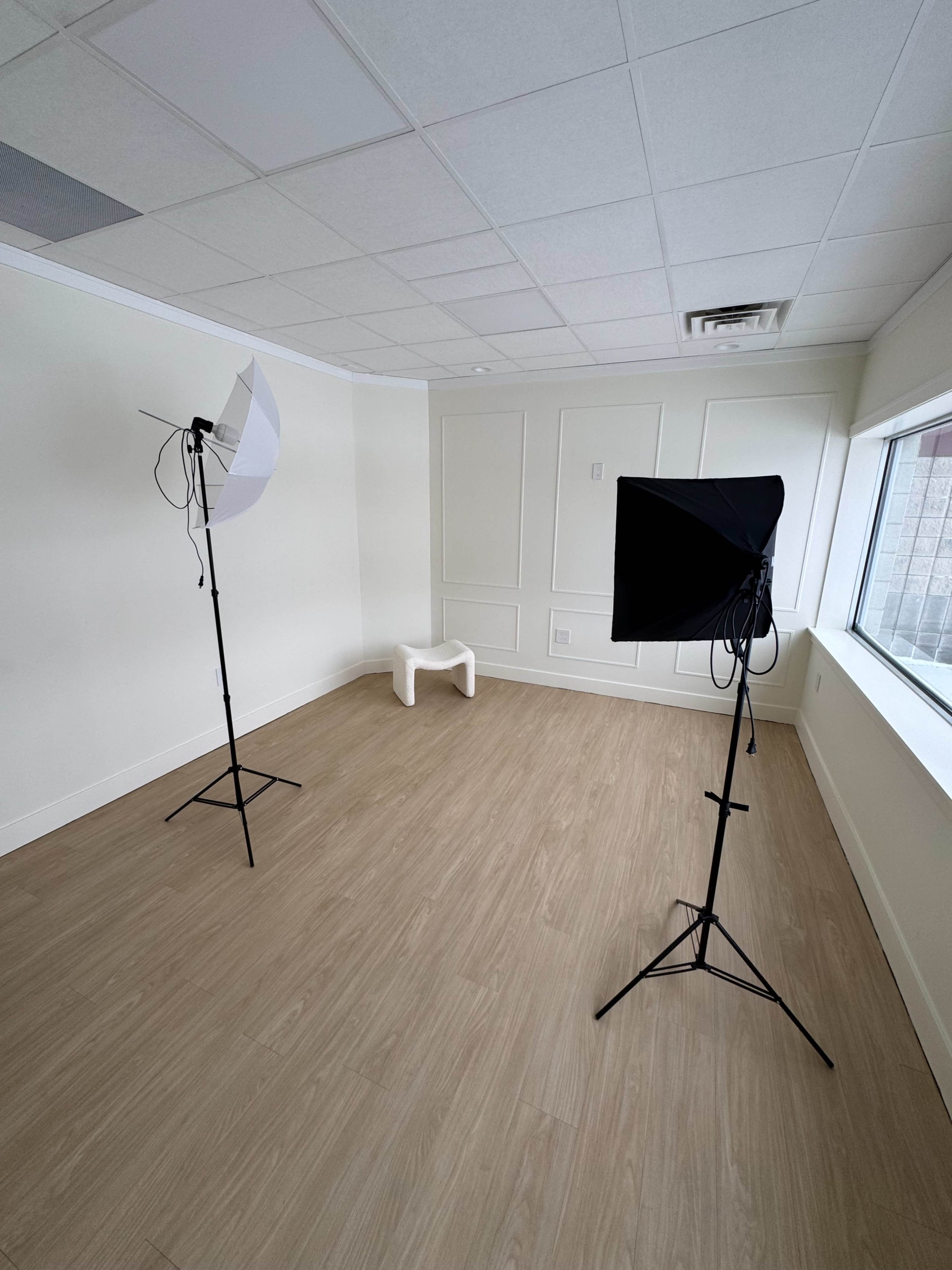 The image shows a vacant room with two light stands and a white bench against a minimally decorated wall.