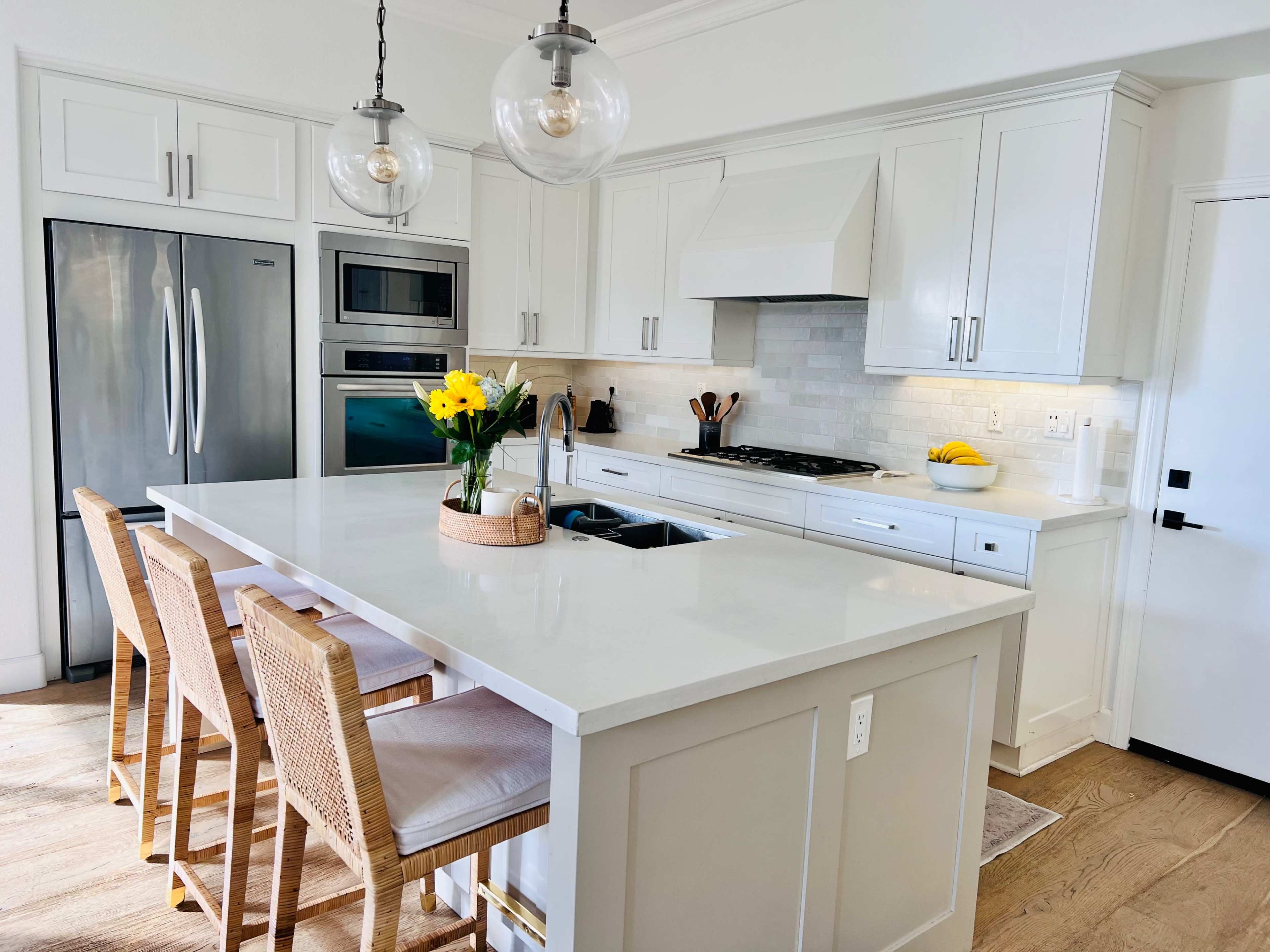 A modern kitchen features white cabinetry, a large island with seating, and stainless steel appliances.