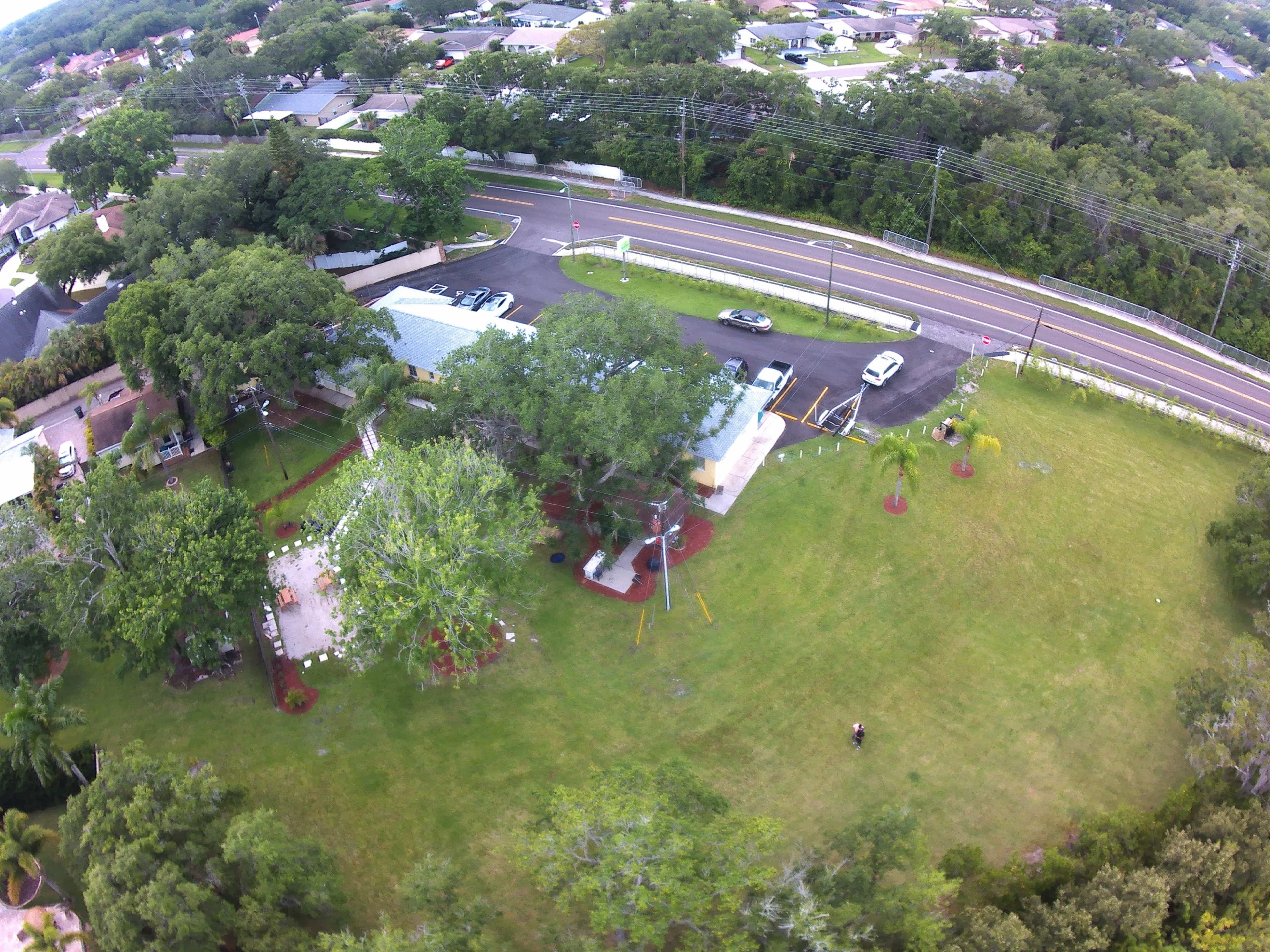 A sprawling green area with a building, several trees, and a road in the background.