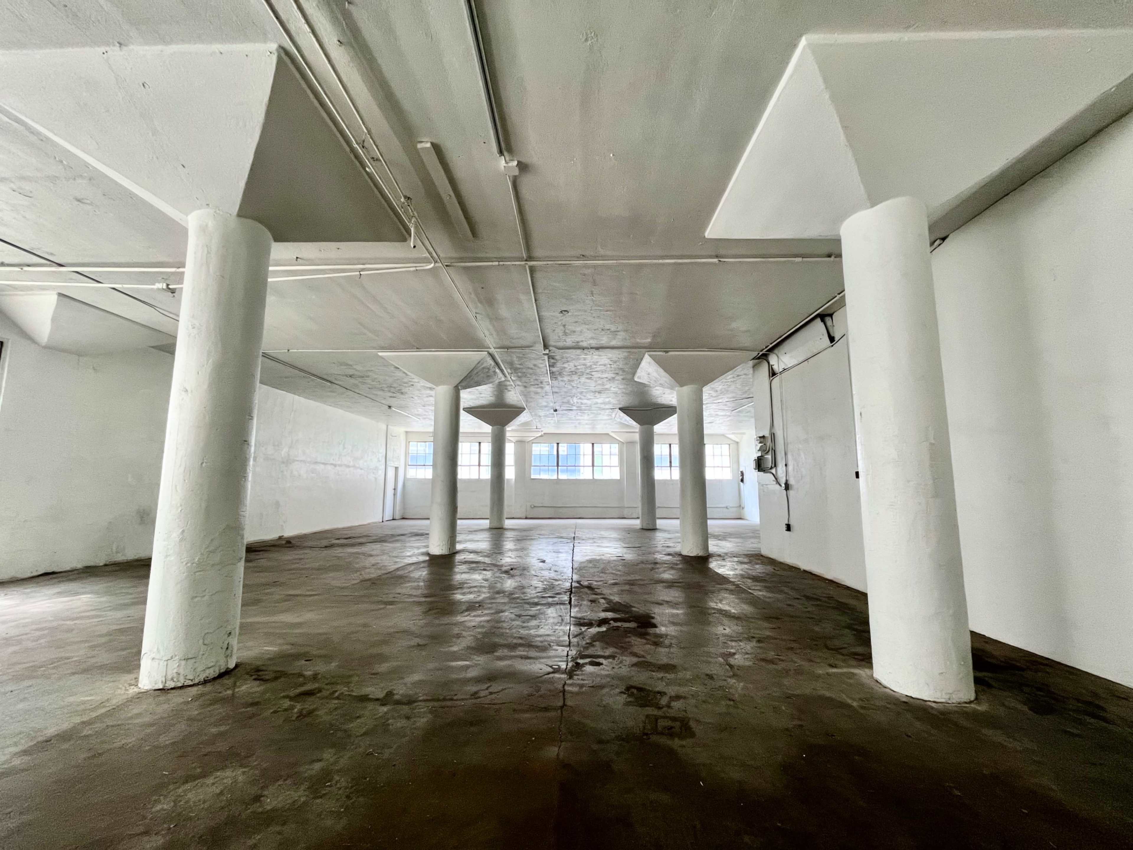 An empty, industrial-style room with concrete floors and several white support pillars.