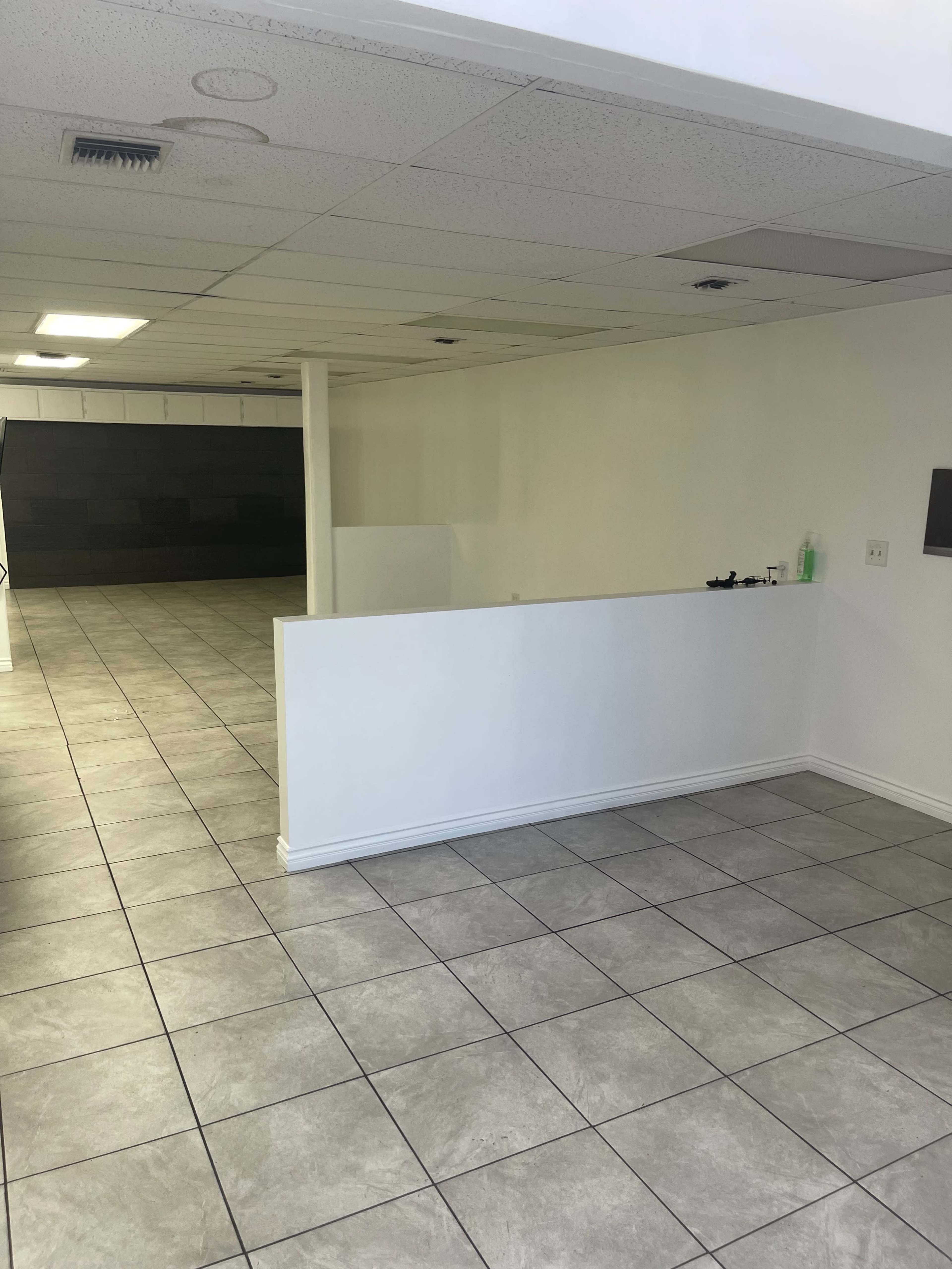 A vacant interior space with tiled flooring, white walls, and a counter area in the foreground.