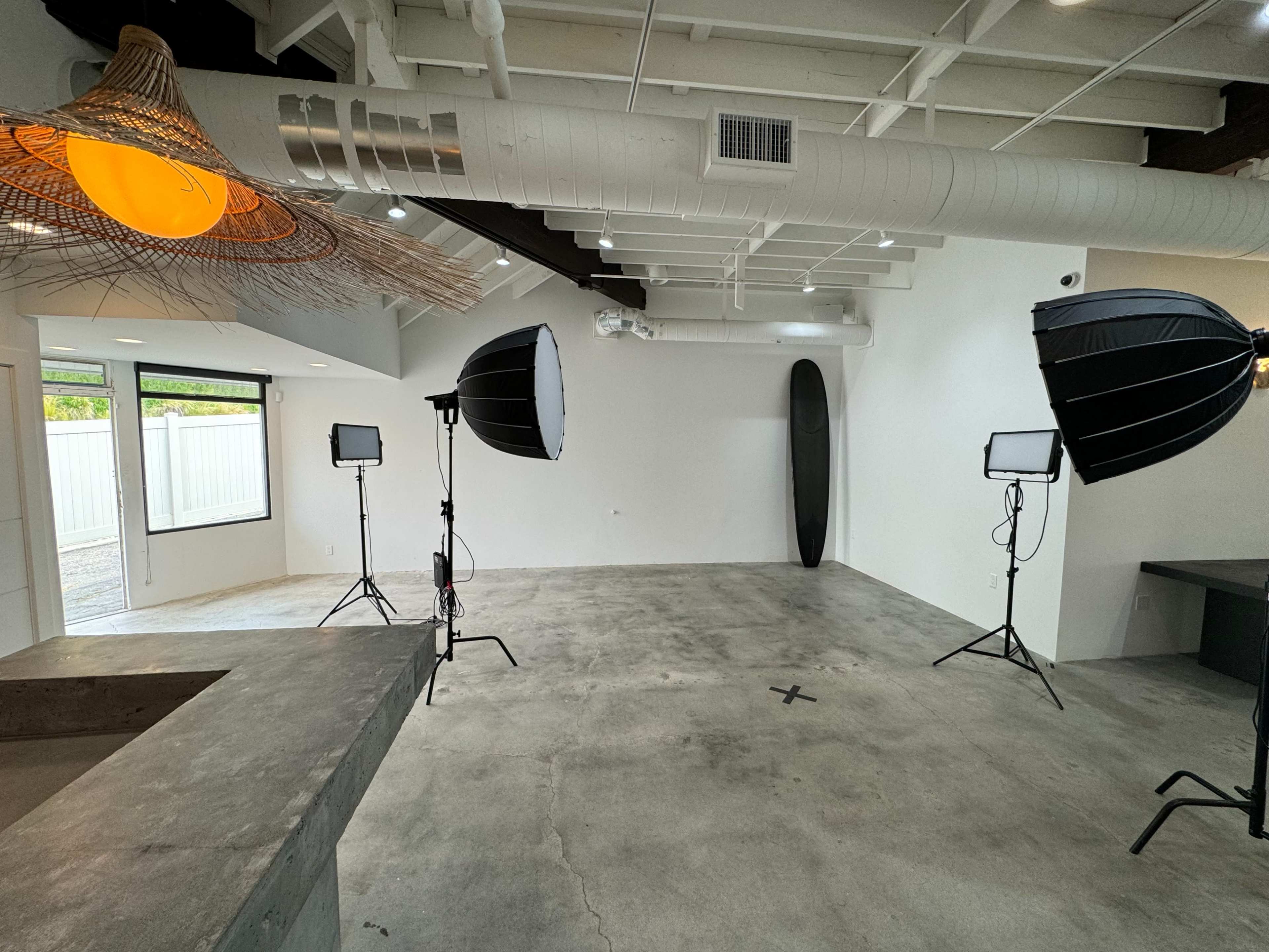 An empty studio space with two softbox lights and a surfboard leaning against the wall.