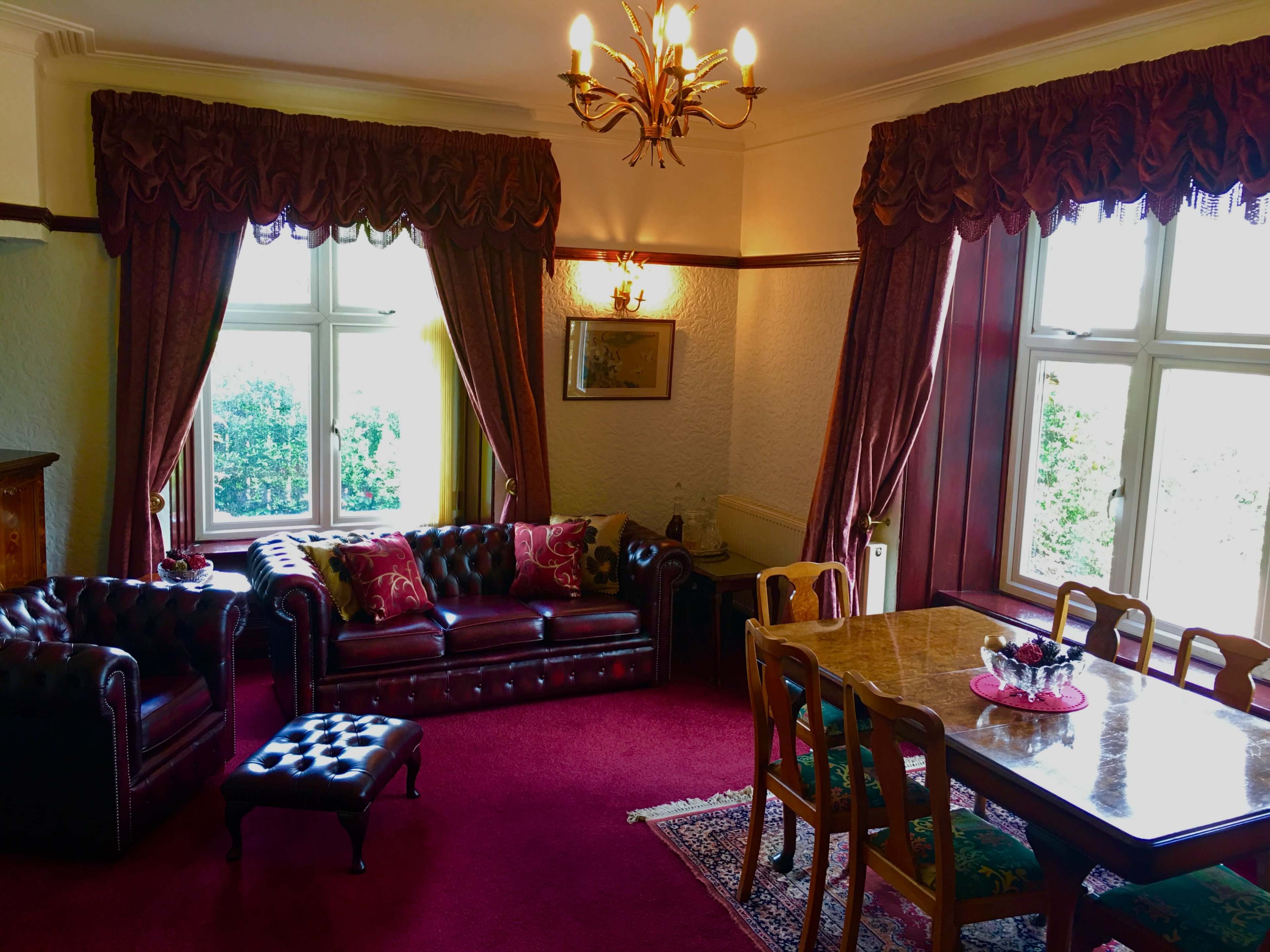 The living room features a leather sofa, an Ottoman, a wooden dining table, and large windows with heavy drapes.