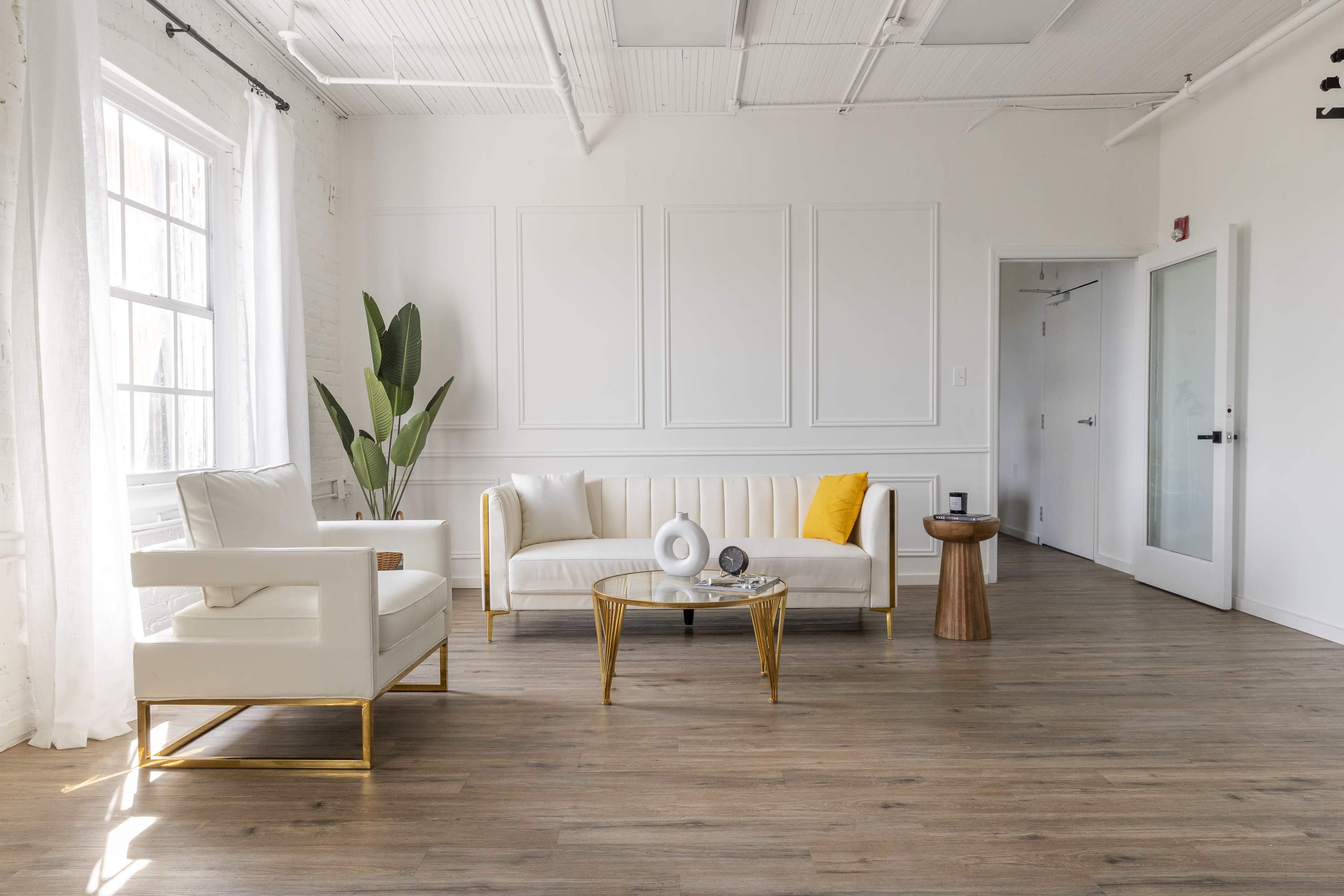 A modern, minimalist living room with a white sofa, a round coffee table, a yellow accent pillow, a plant, and a wooden side table.