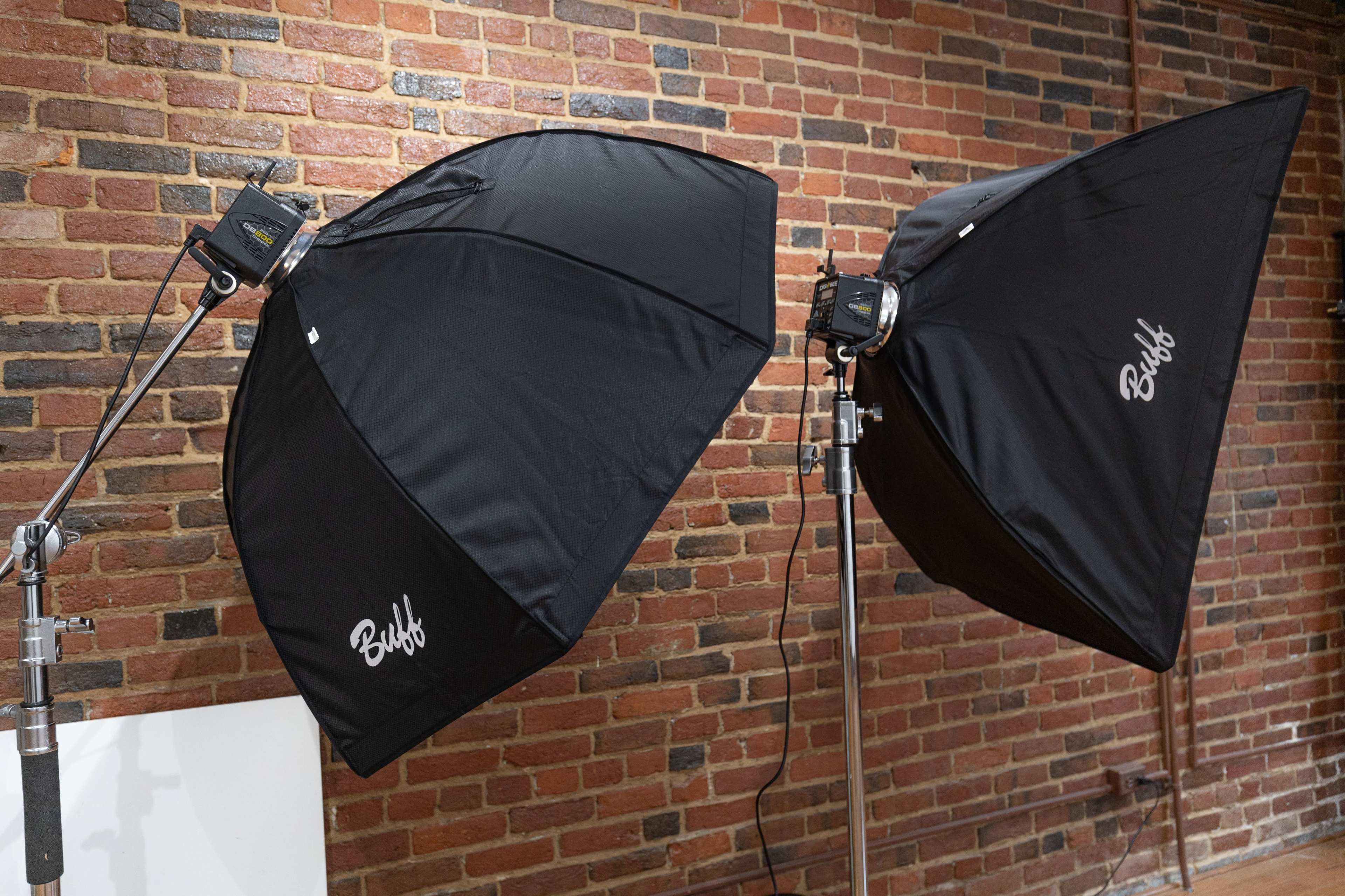 Two softbox lights are positioned on stands against a brick wall.