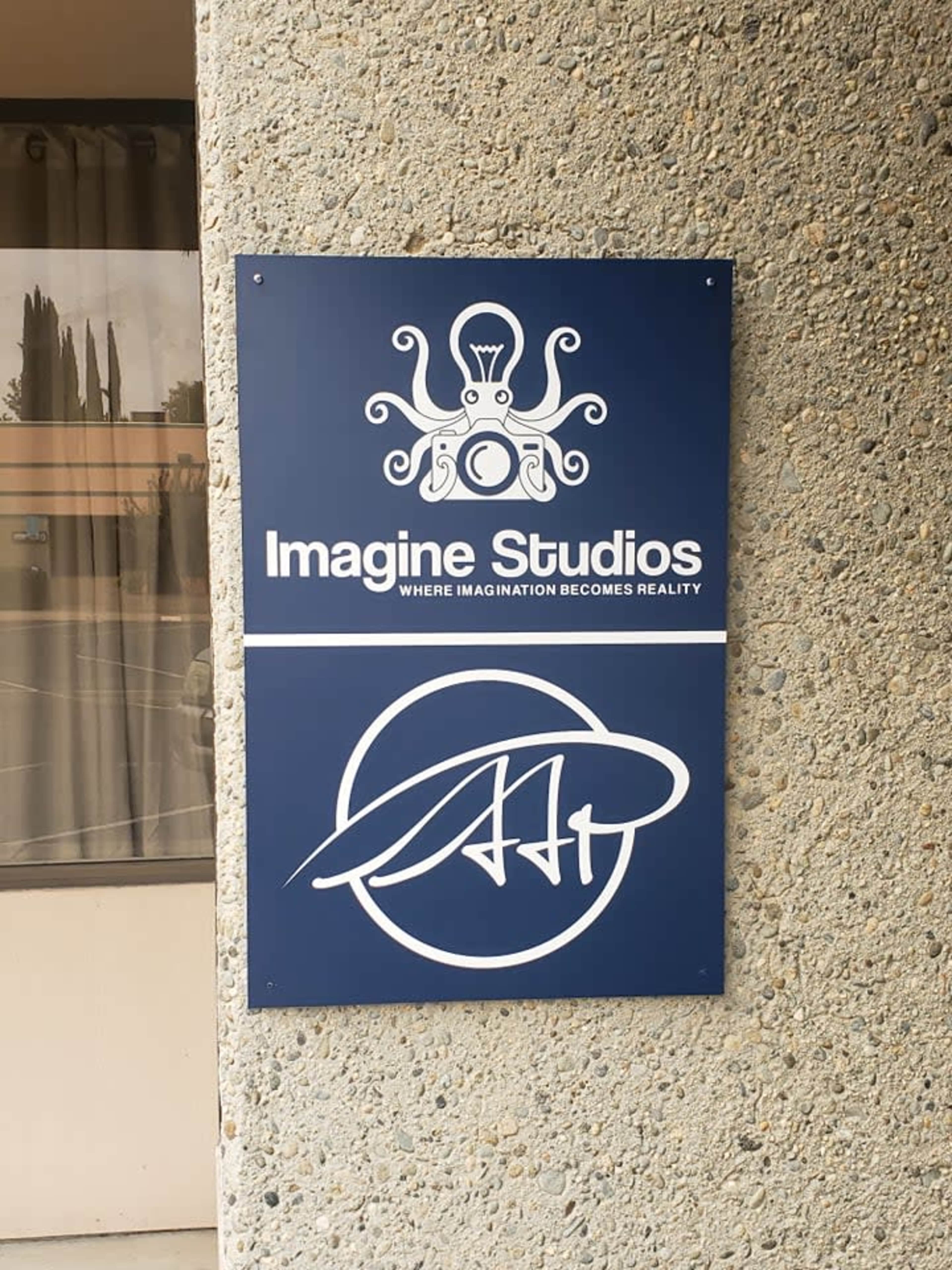A sign for Imagine Studios featuring an octopus graphic and the tagline "WHERE IMAGINATION BECOMES REALITY" hangs on a textured gray wall.
