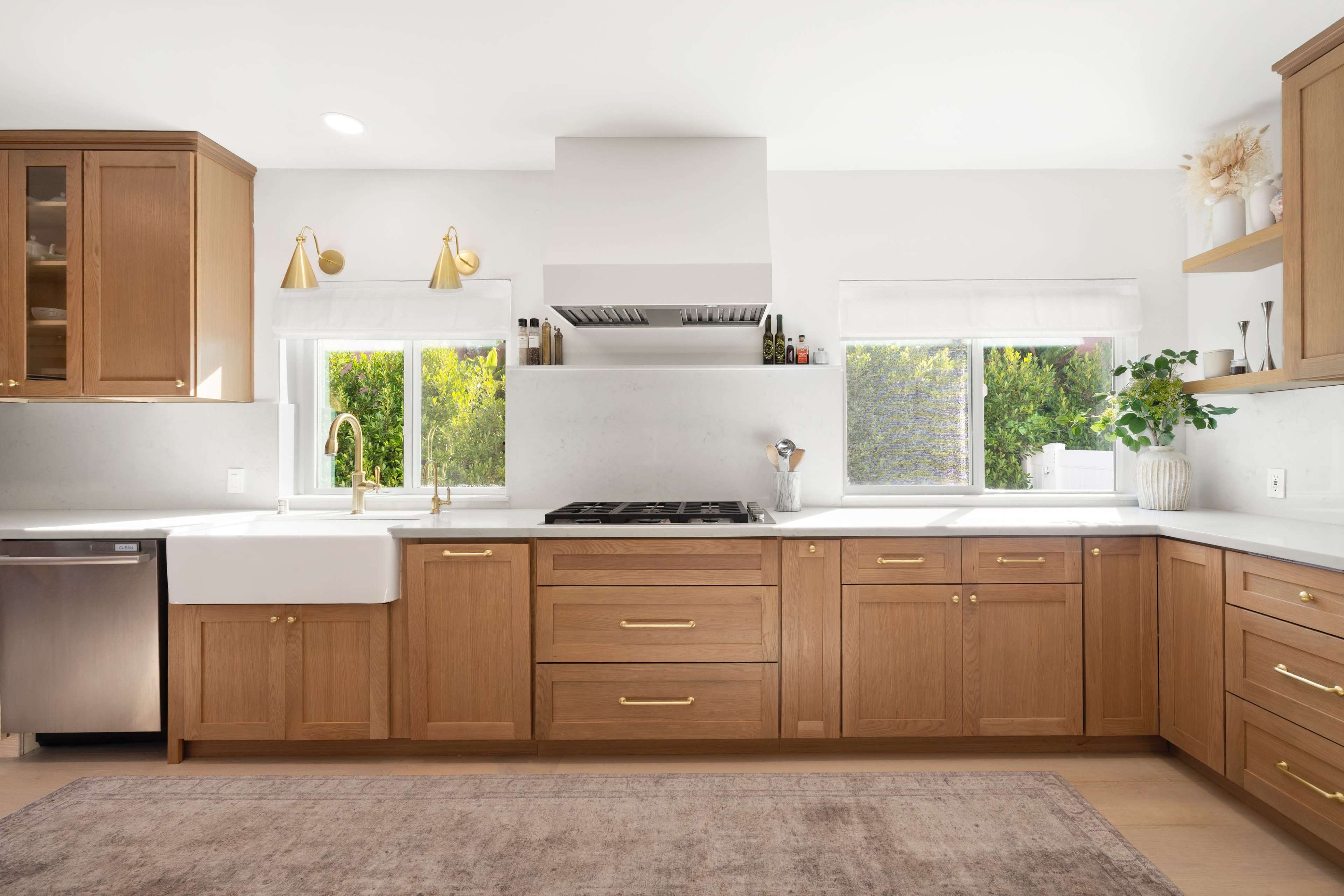 The kitchen features wooden cabinetry, a white countertop, a farmhouse sink, and large windows providing natural light.