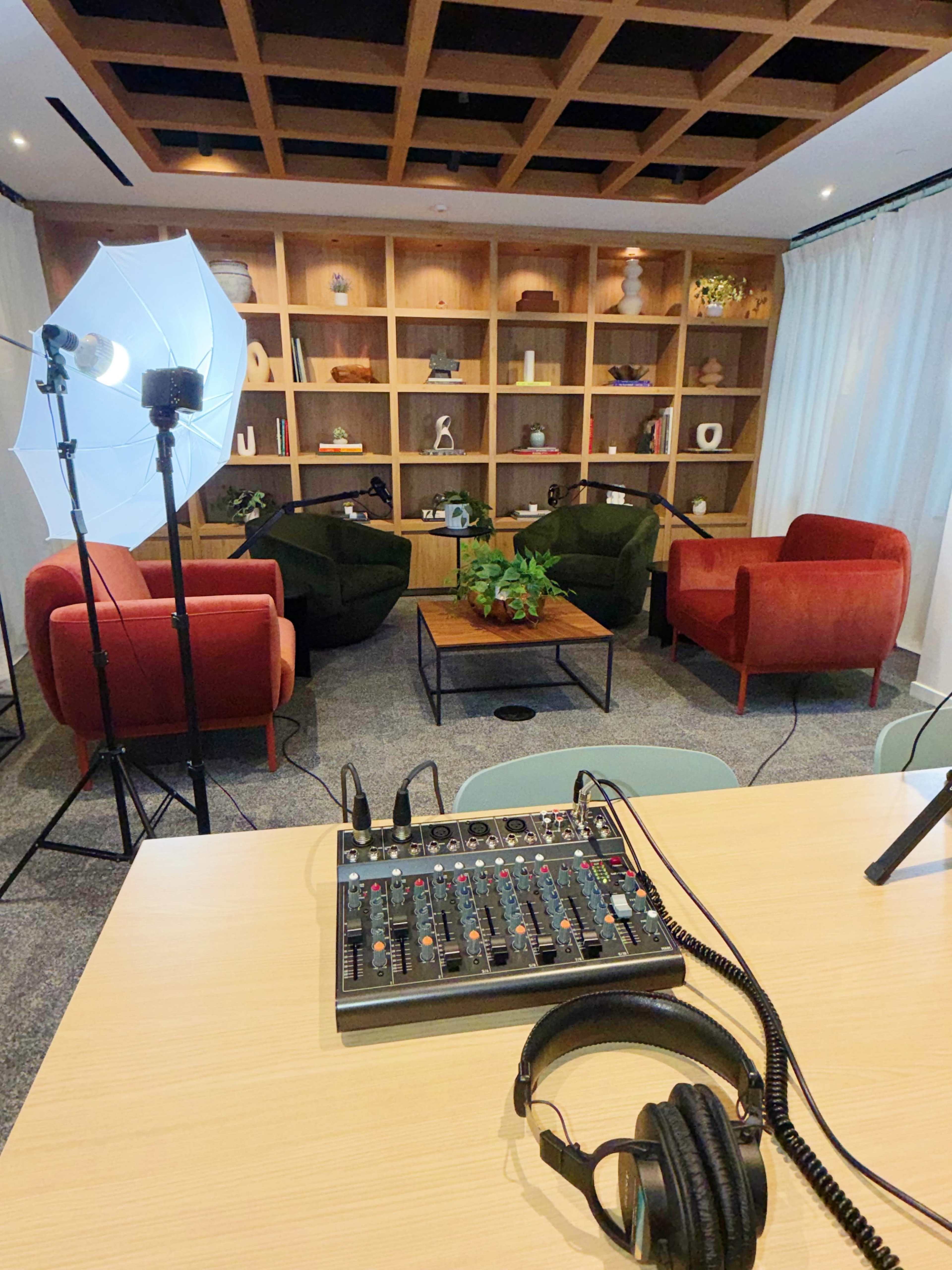 The image features a modern recording space with two chairs, a coffee table, and a sound mixing console set up for audio recording.