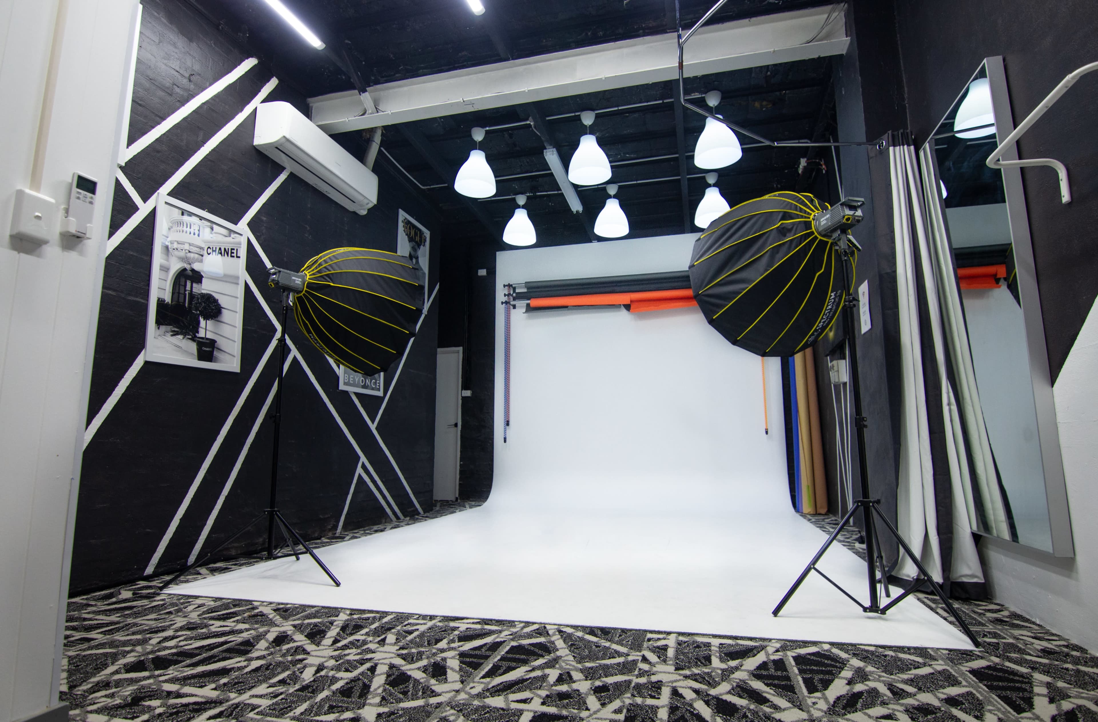 A photography studio featuring a white backdrop, two large octagonal softboxes, and patterned flooring.