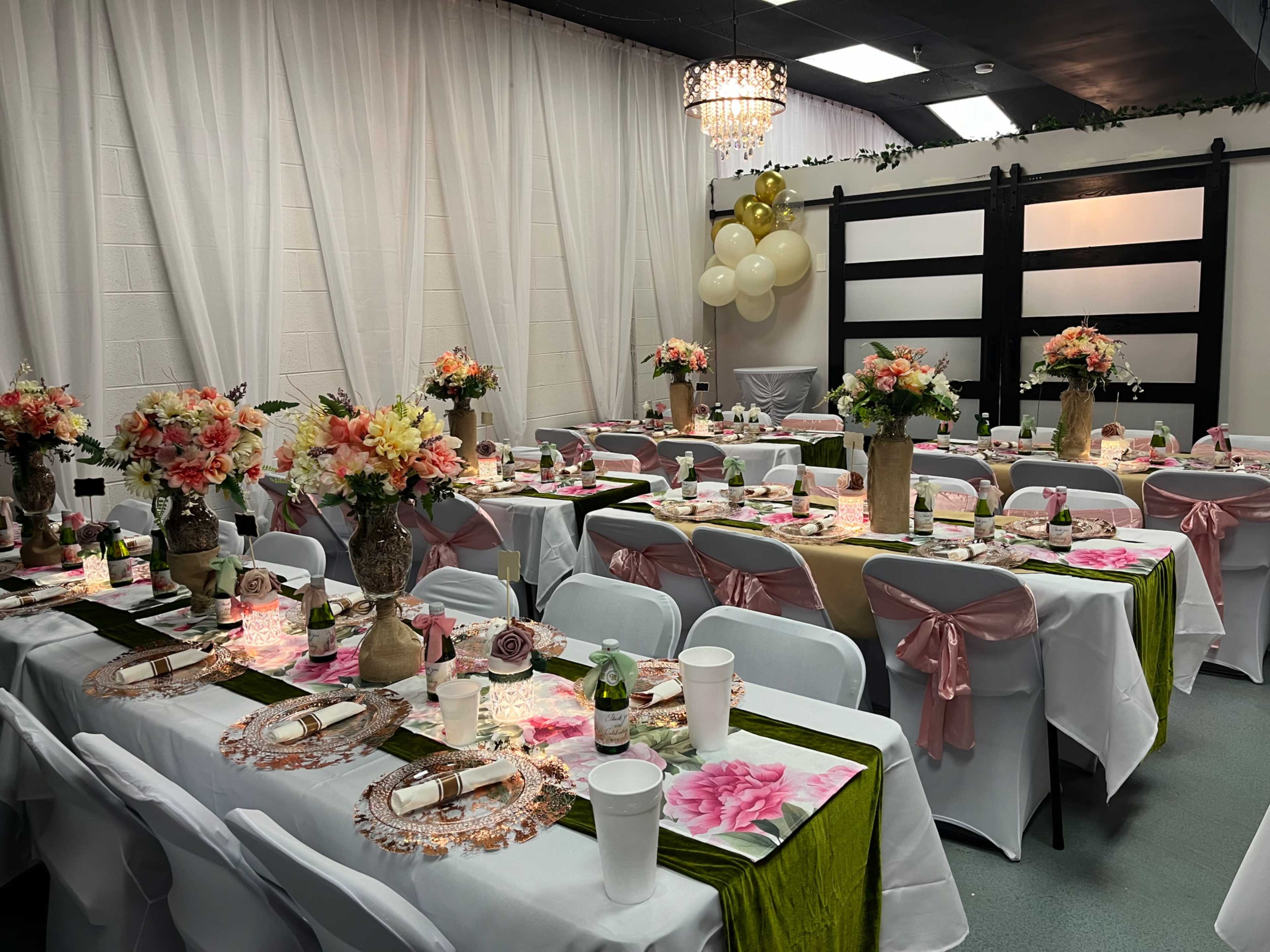 The image shows a banquet hall set up with multiple tables decorated with floral centerpieces, plates, and drinks, arranged for an event.