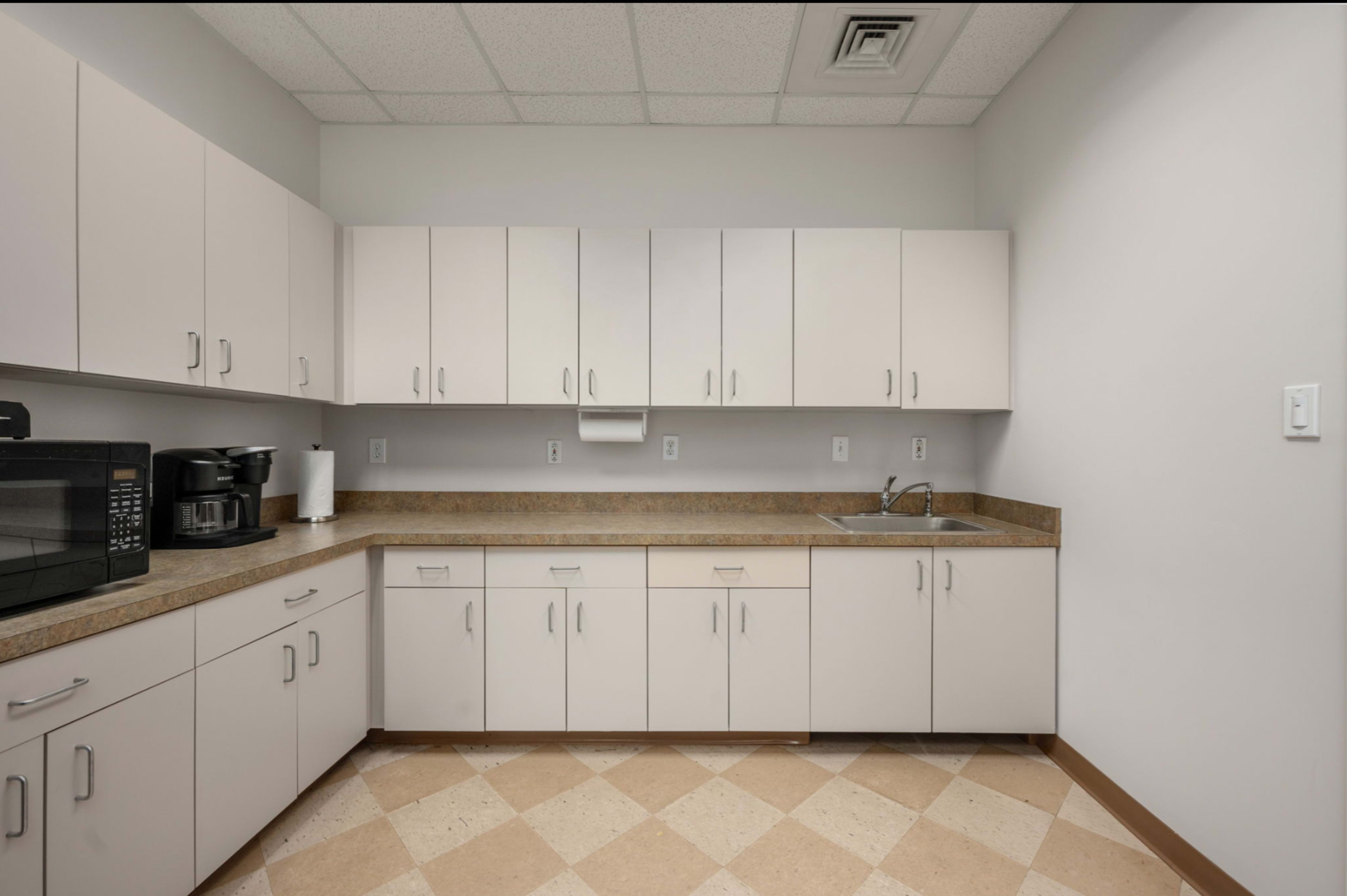 The image shows a clean, modern kitchen space with beige cabinets, a sink, and a microwave.