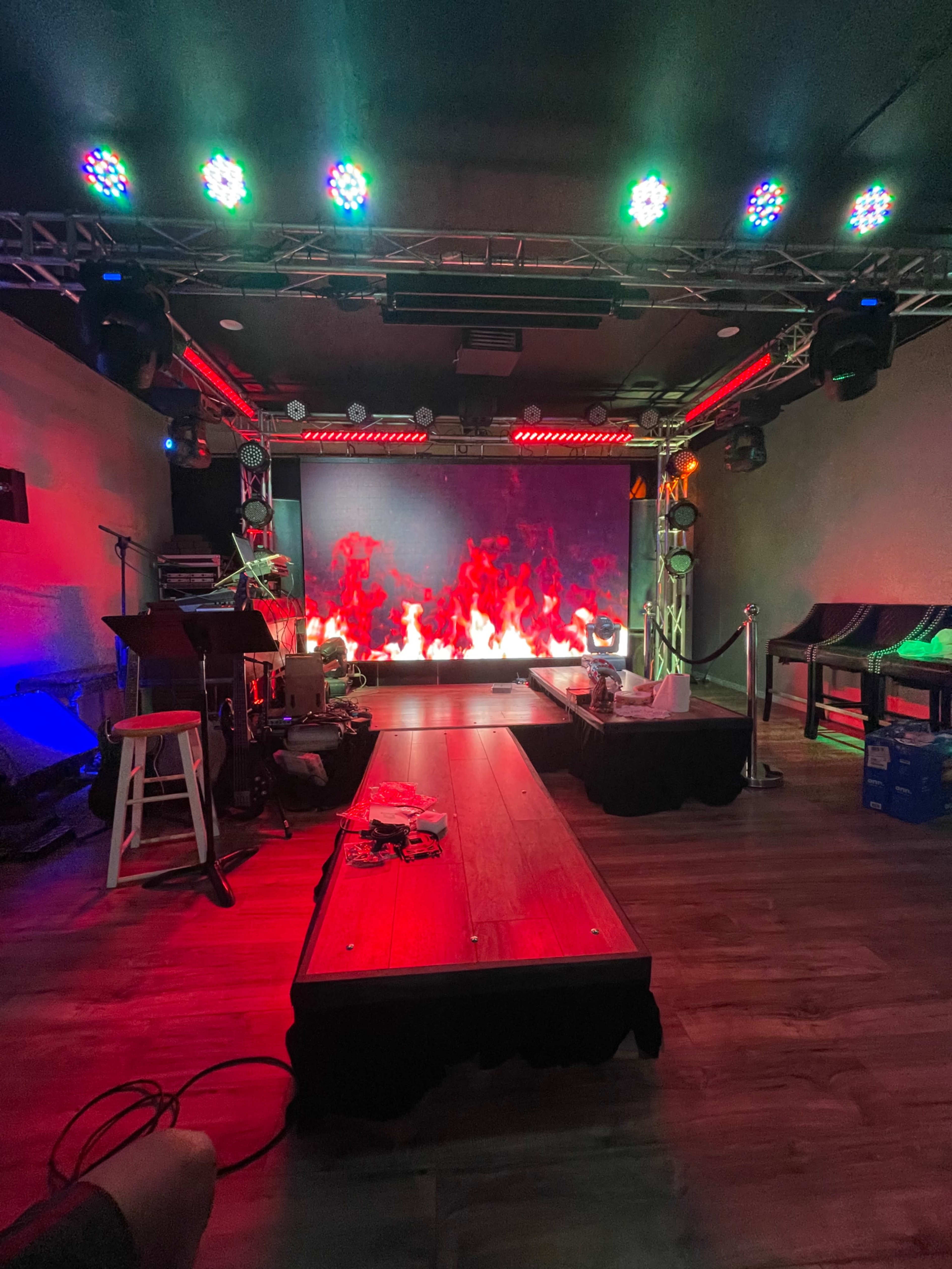 A performance stage with a backdrop of digital flames, surrounded by colorful stage lights and equipment.