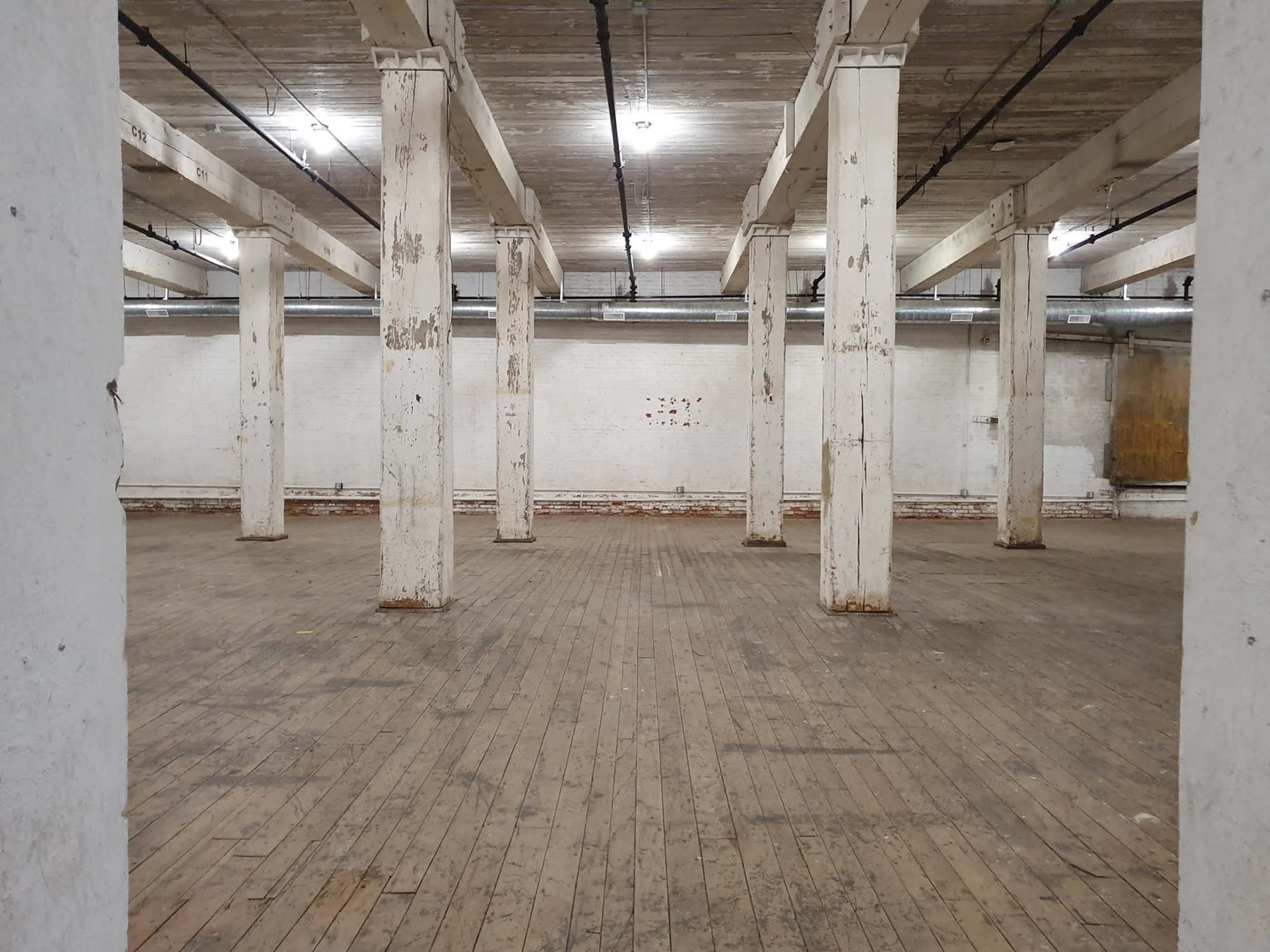 An empty warehouse interior with wooden floors and supporting columns.