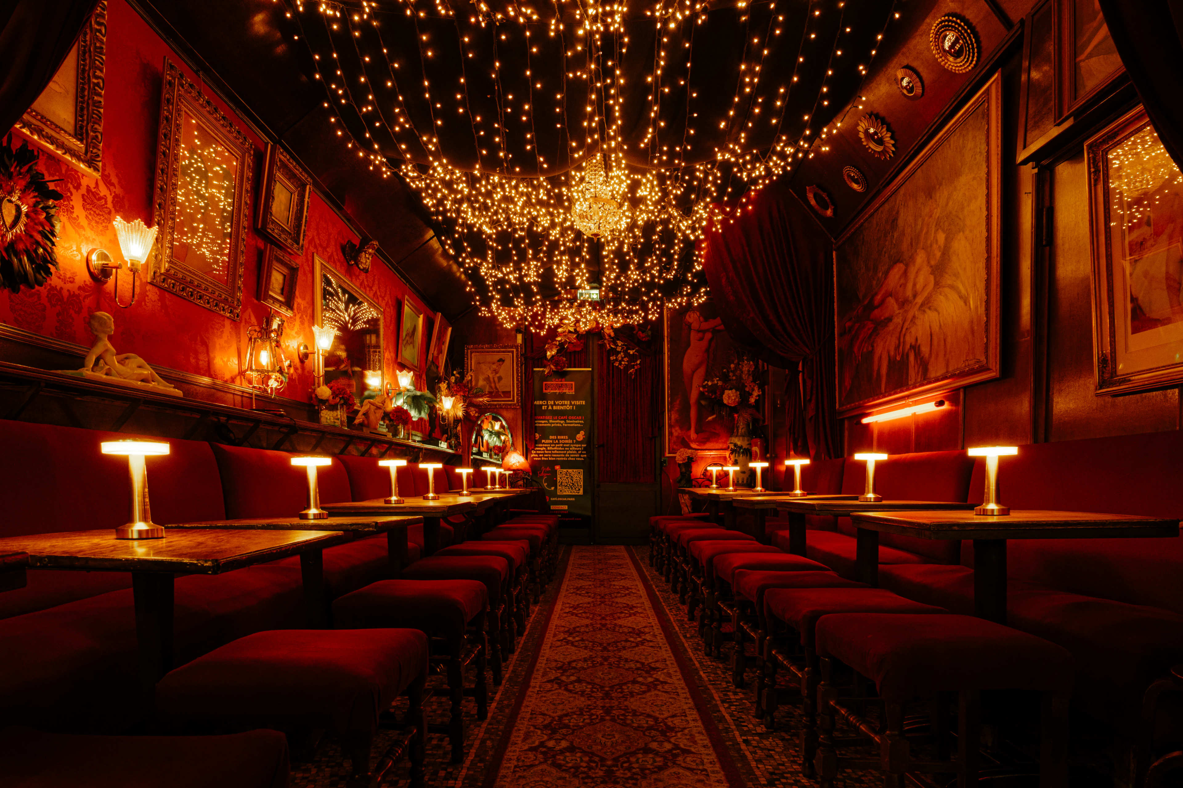 The image shows an elegantly decorated dimly lit interior of a restaurant or lounge with red seating and numerous string lights hanging from the ceiling.