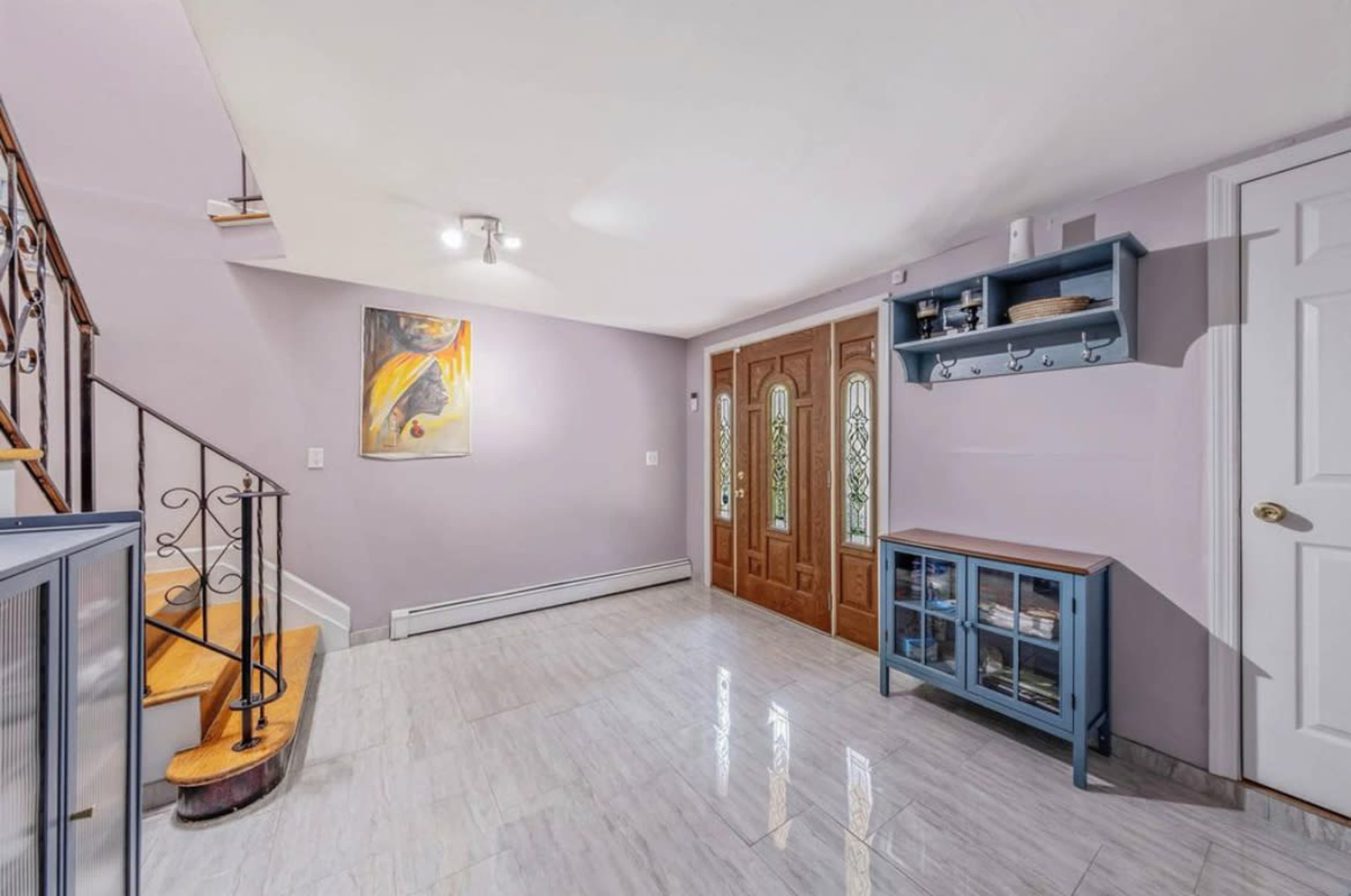The image shows a well-lit entryway with a staircase, two decorative doors, and a blue storage cabinet.