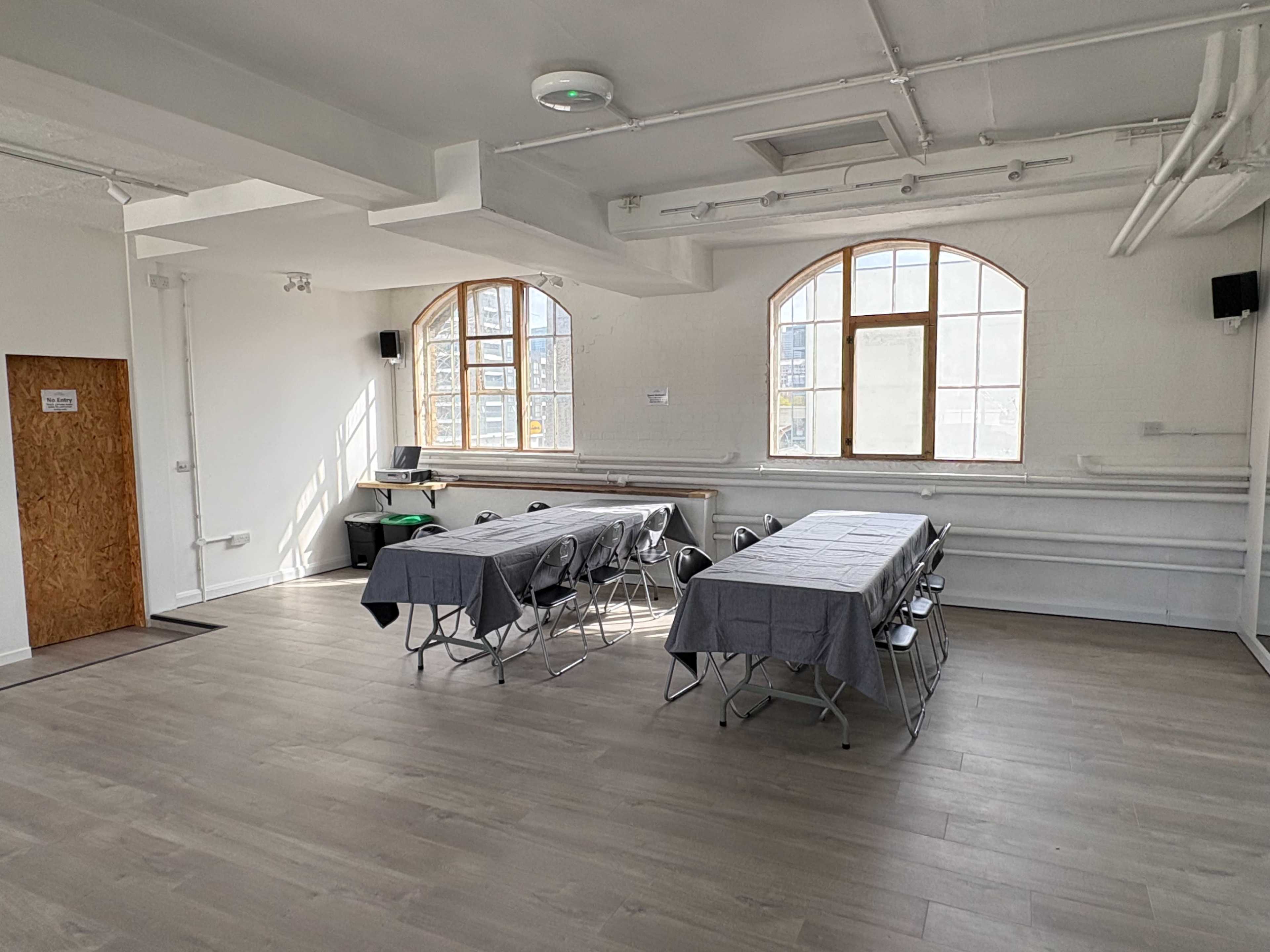 The room features two sets of rectangular tables with gray tablecloths, arranged in a spacious area with large windows allowing natural light.