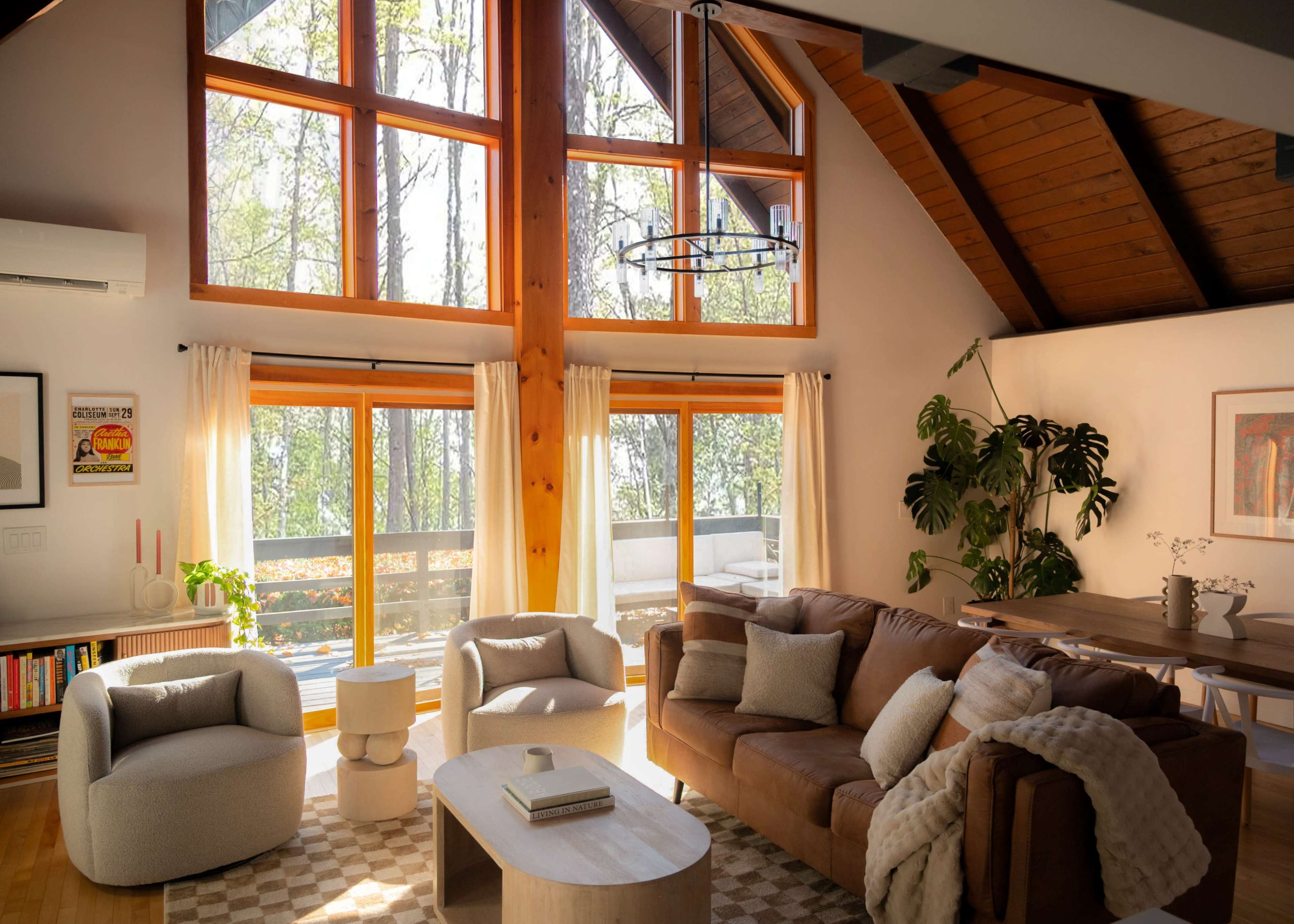 A modern living room features a large sectional sofa, two circular armchairs, and a central coffee table, all set against windows that provide natural light and a view of the outdoors.